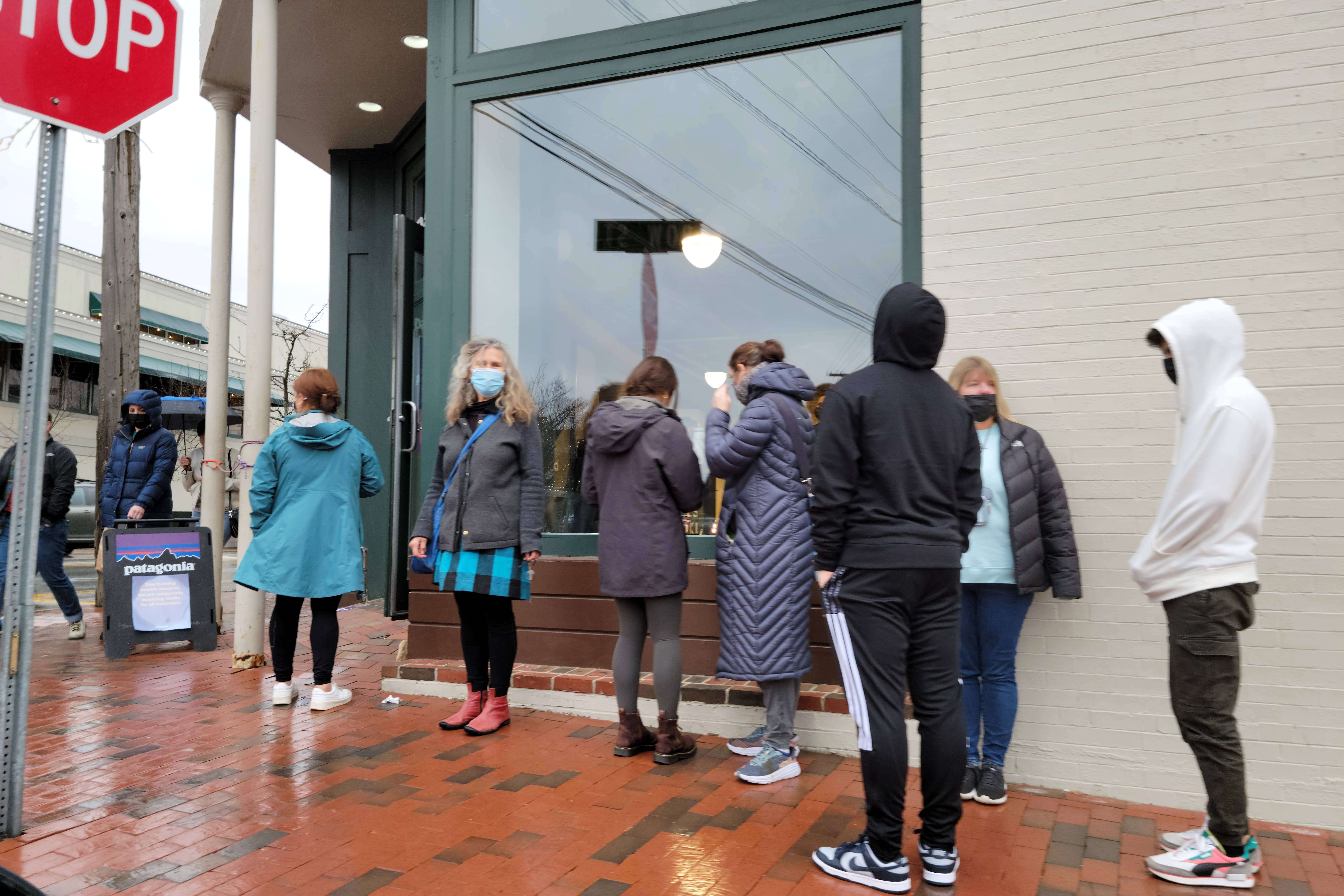 people standing in line at street corner outside of a retail store entrance