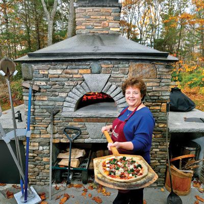 Jill Strauss holds a Neapolitan pizza in front of the wood-fired oven where she hosts backyard classes on how to make pizza.
