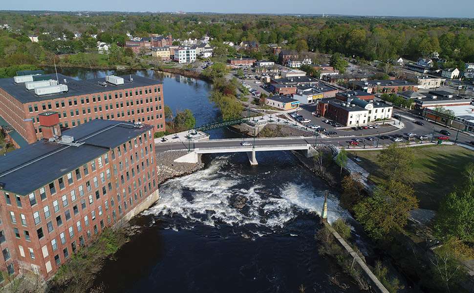 an aerial photo of a mill along a river with downtown Westbrook surrounding it