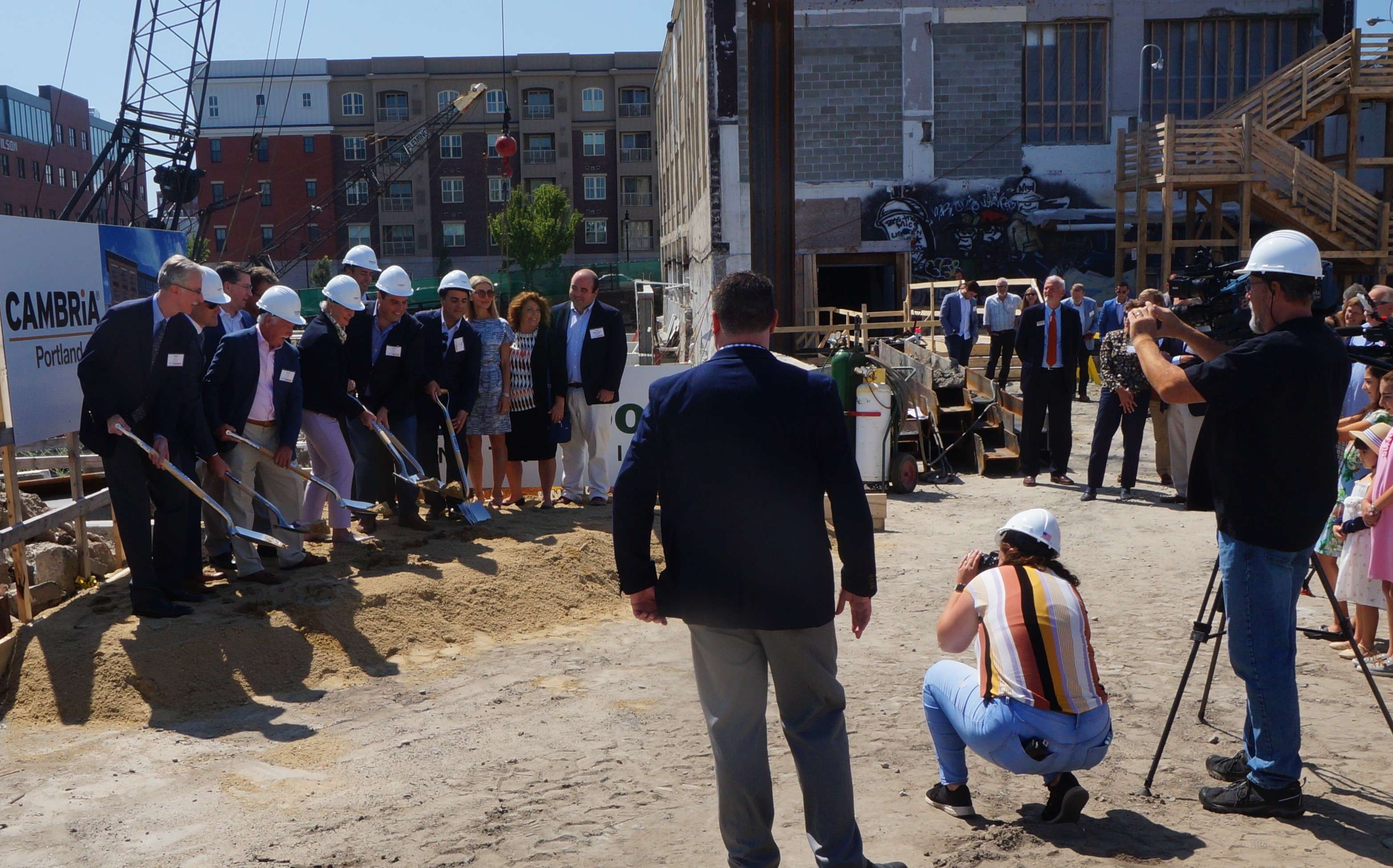 A large group of people shovels dirt in front of a city construction site