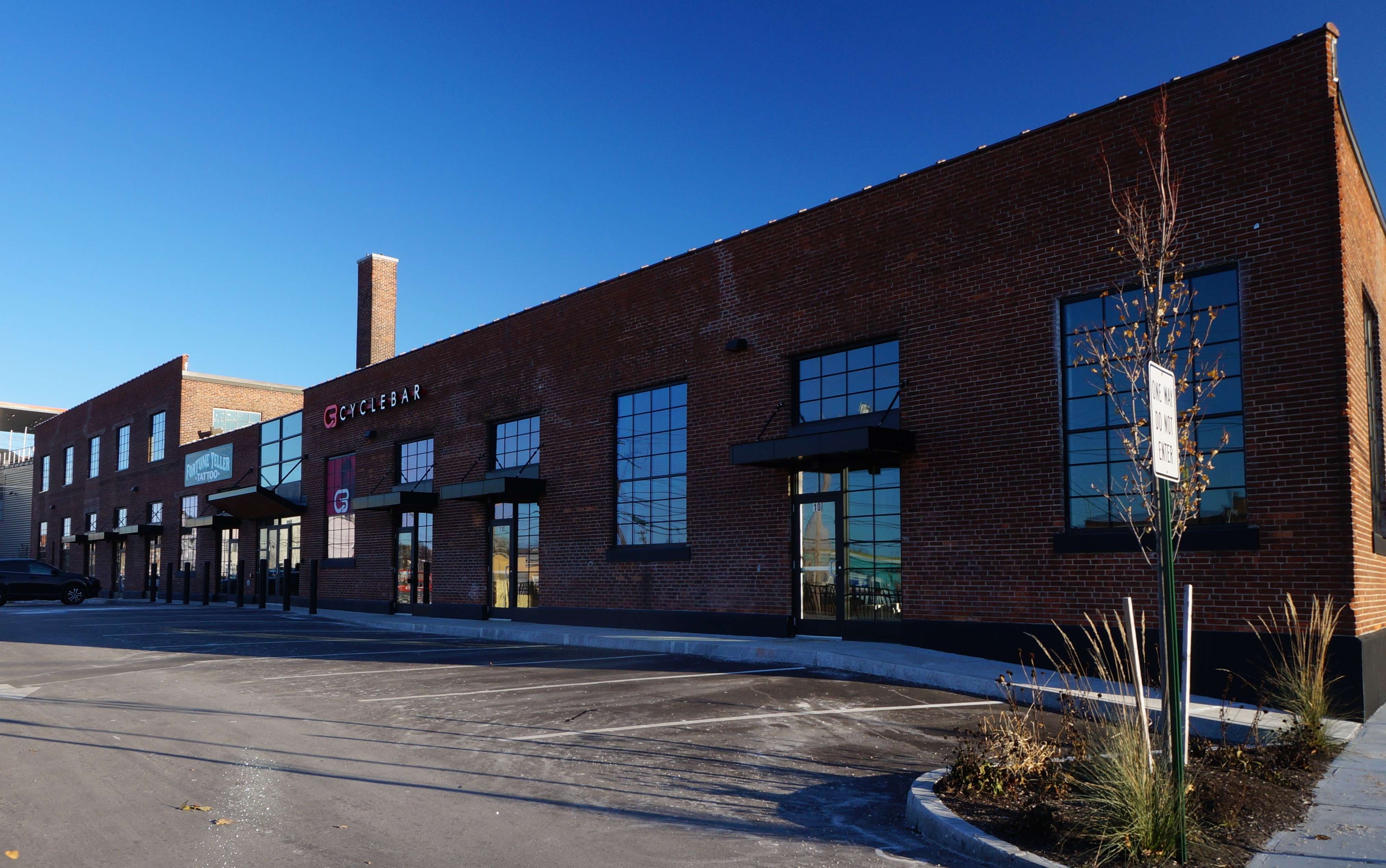 A one and two story long brick building with a parking lot in front and a big sign that says Cycle Bar.