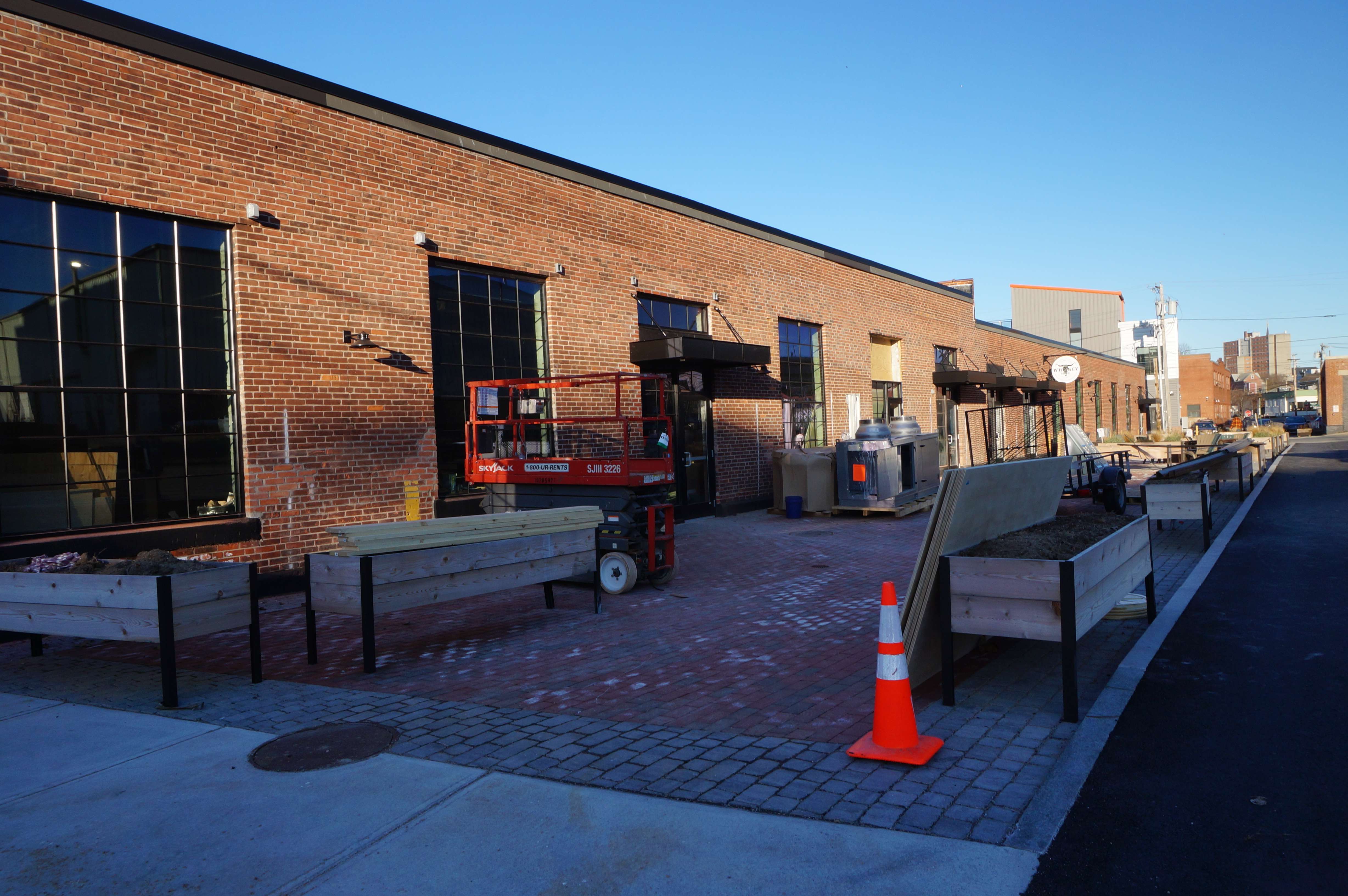 A long brick building with a patio along the front and construction equipment in the foreground.
