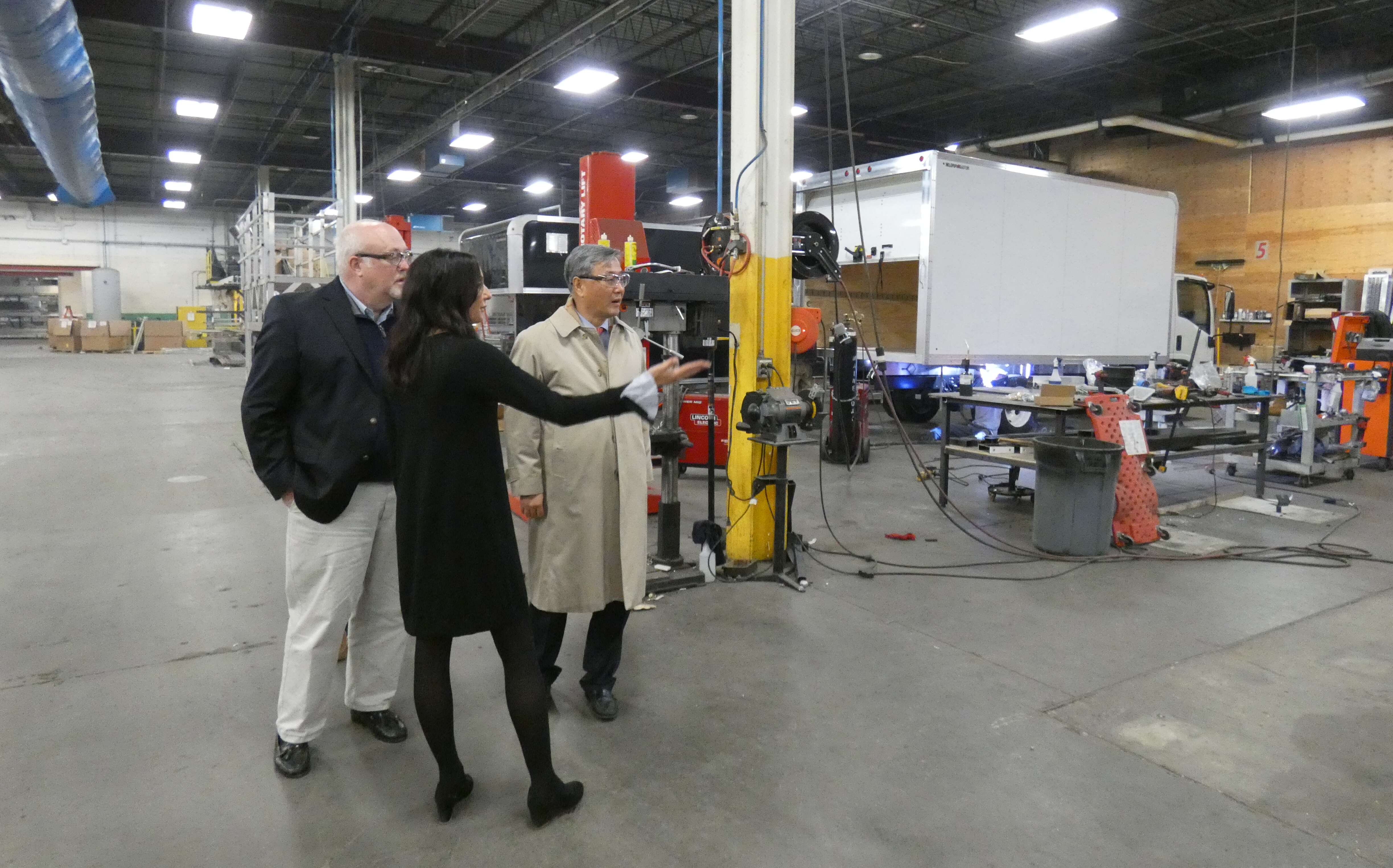 A woman and two men in discussion on the floor of a large manufacturing plant.