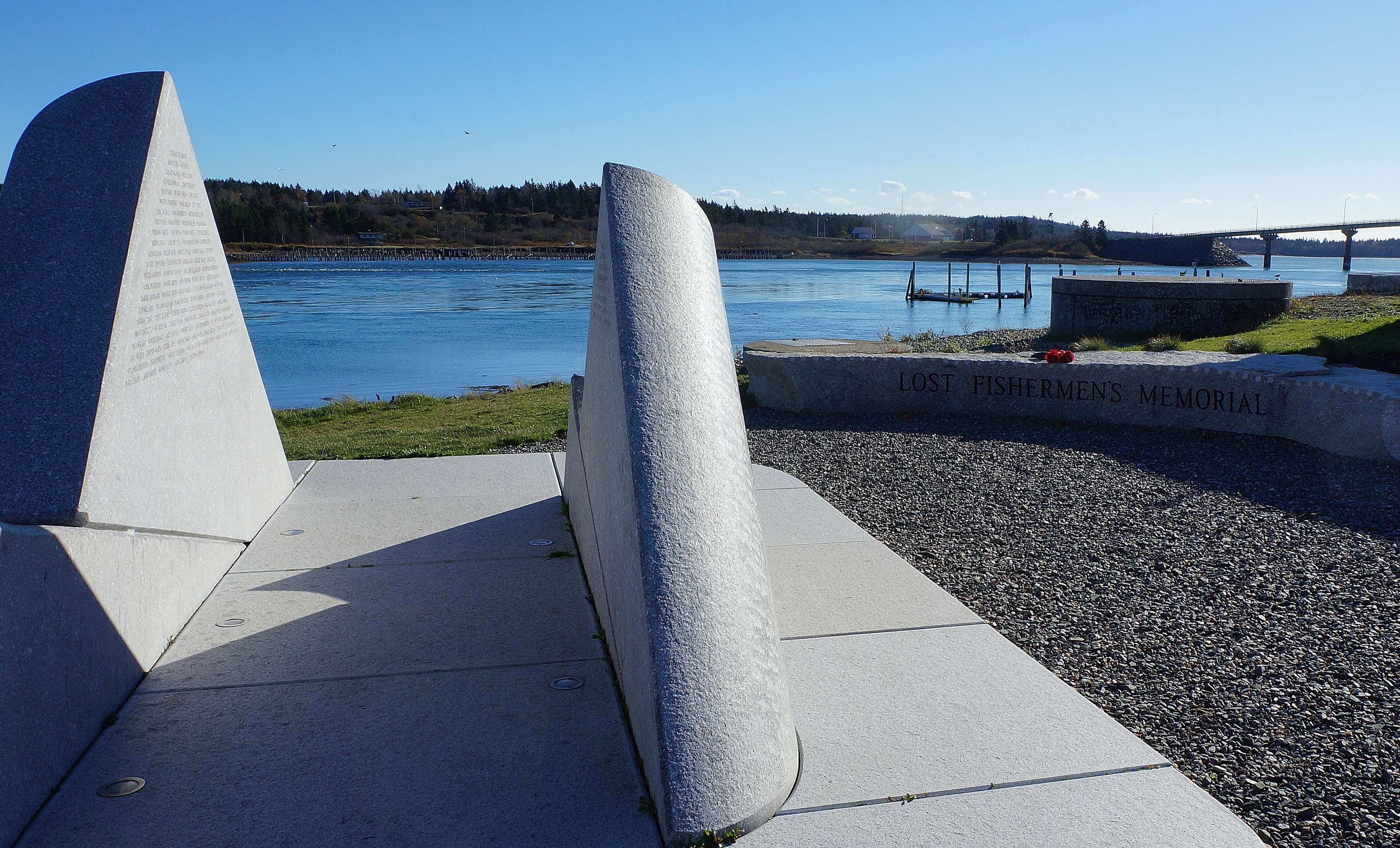 A granite memorial shaped like ocean waves with names on it and the ocean in the background