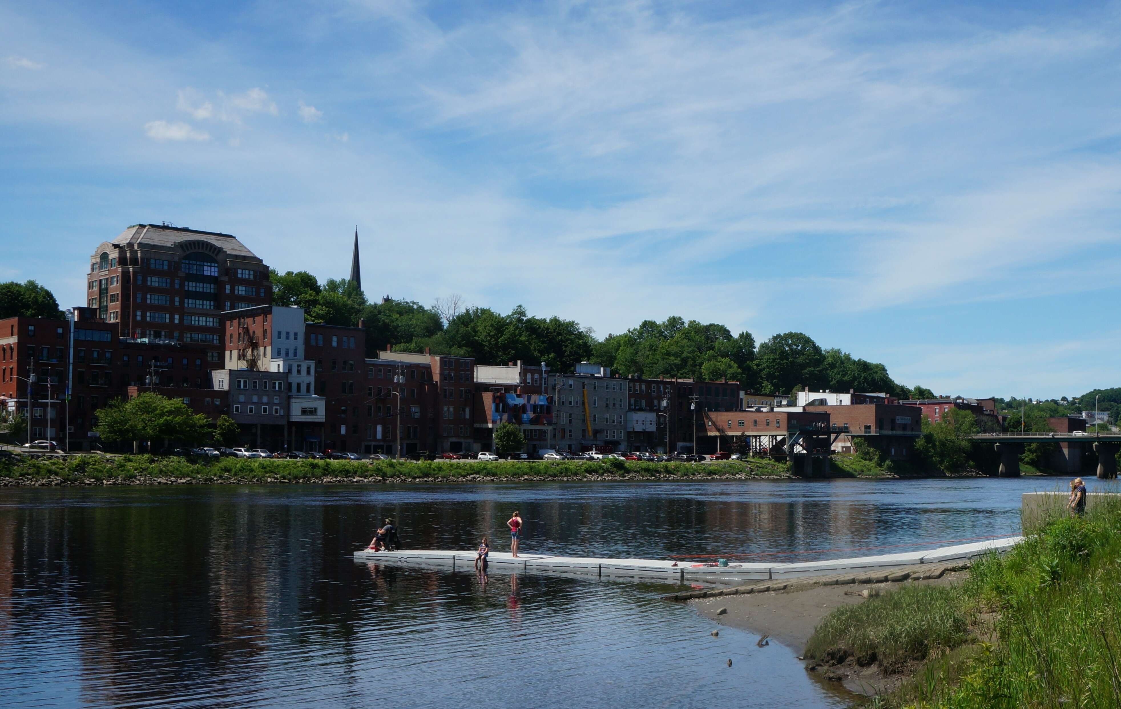 People fish of a dock on a wide river, with a downtown on the other side