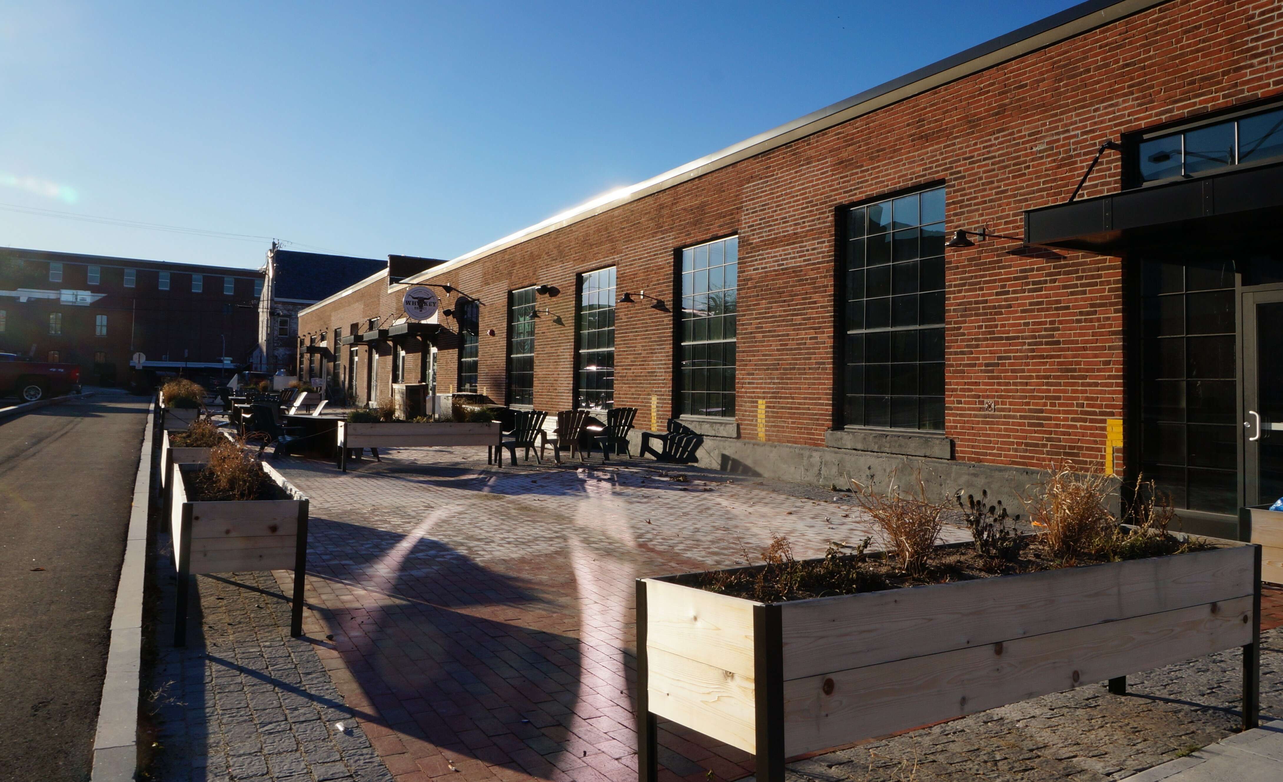 A long brick courtyard in front of a low brick industrial building with lots of big windows