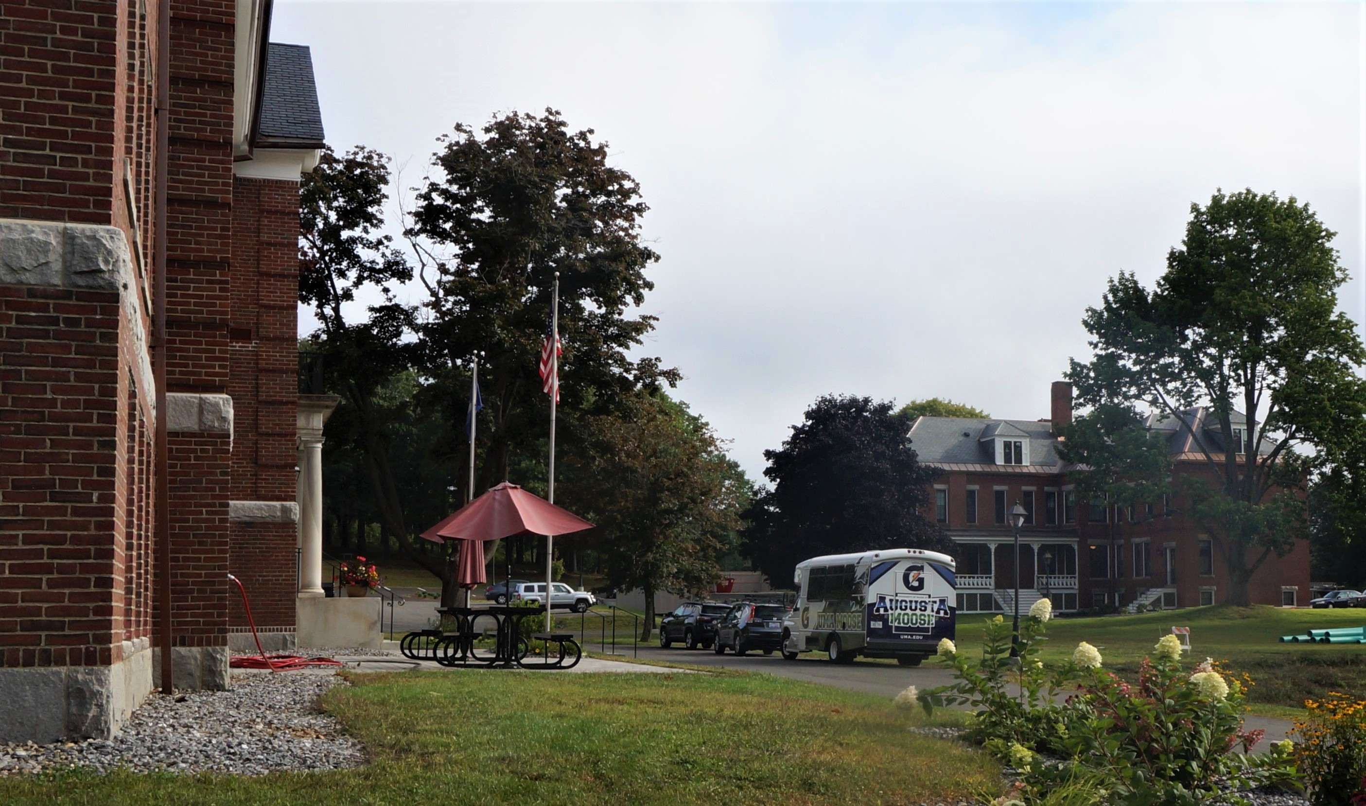 Part of a brick building in the foreground and across a landscaped lawn another three-story brick building in the back and shuttle bus that says Augusta Moose on it
