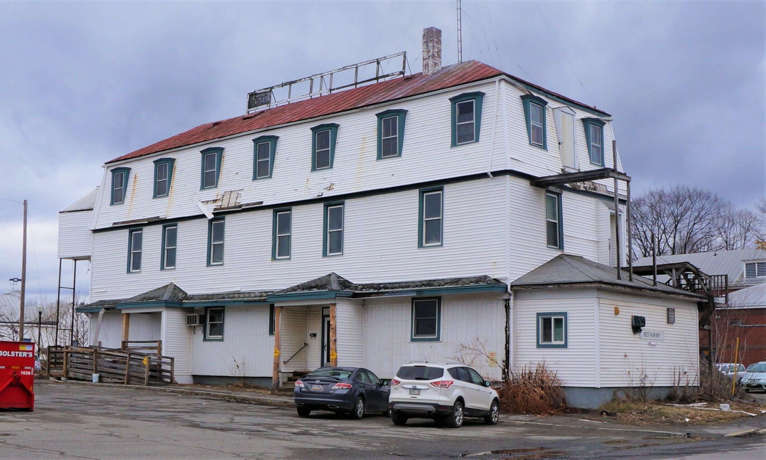 A three-story large white dilapidated buiding with shingles falling off