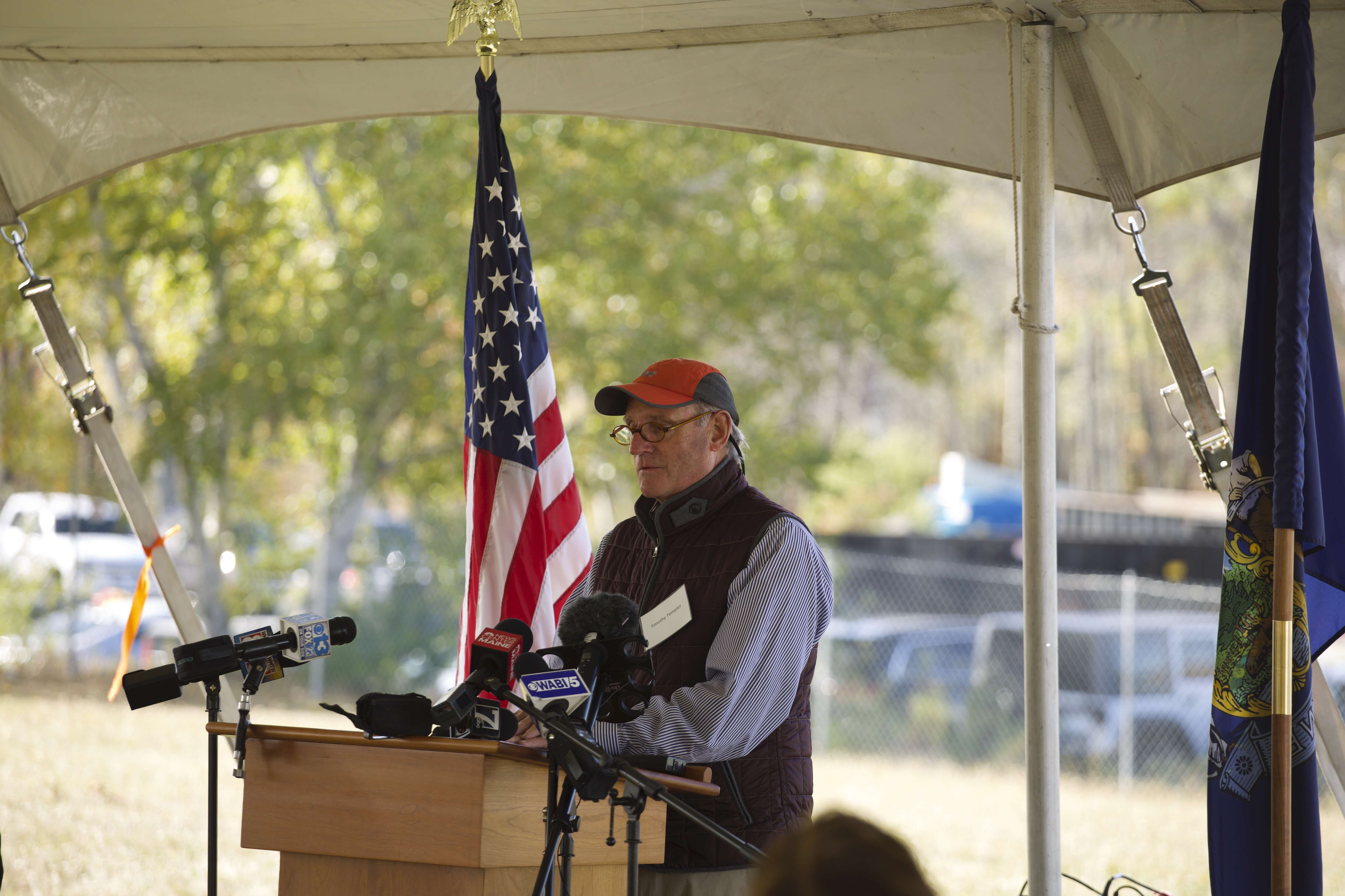 a man, white, speaks at a lecturn outdoors