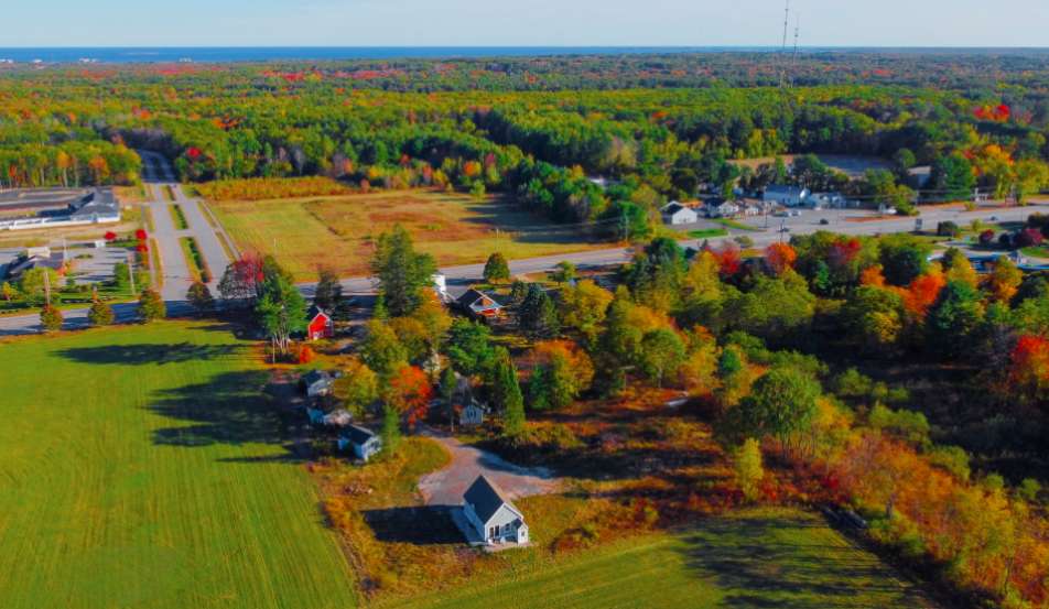 an aerial view showing green fields and trees with fall foliage, and the ocean in the distance