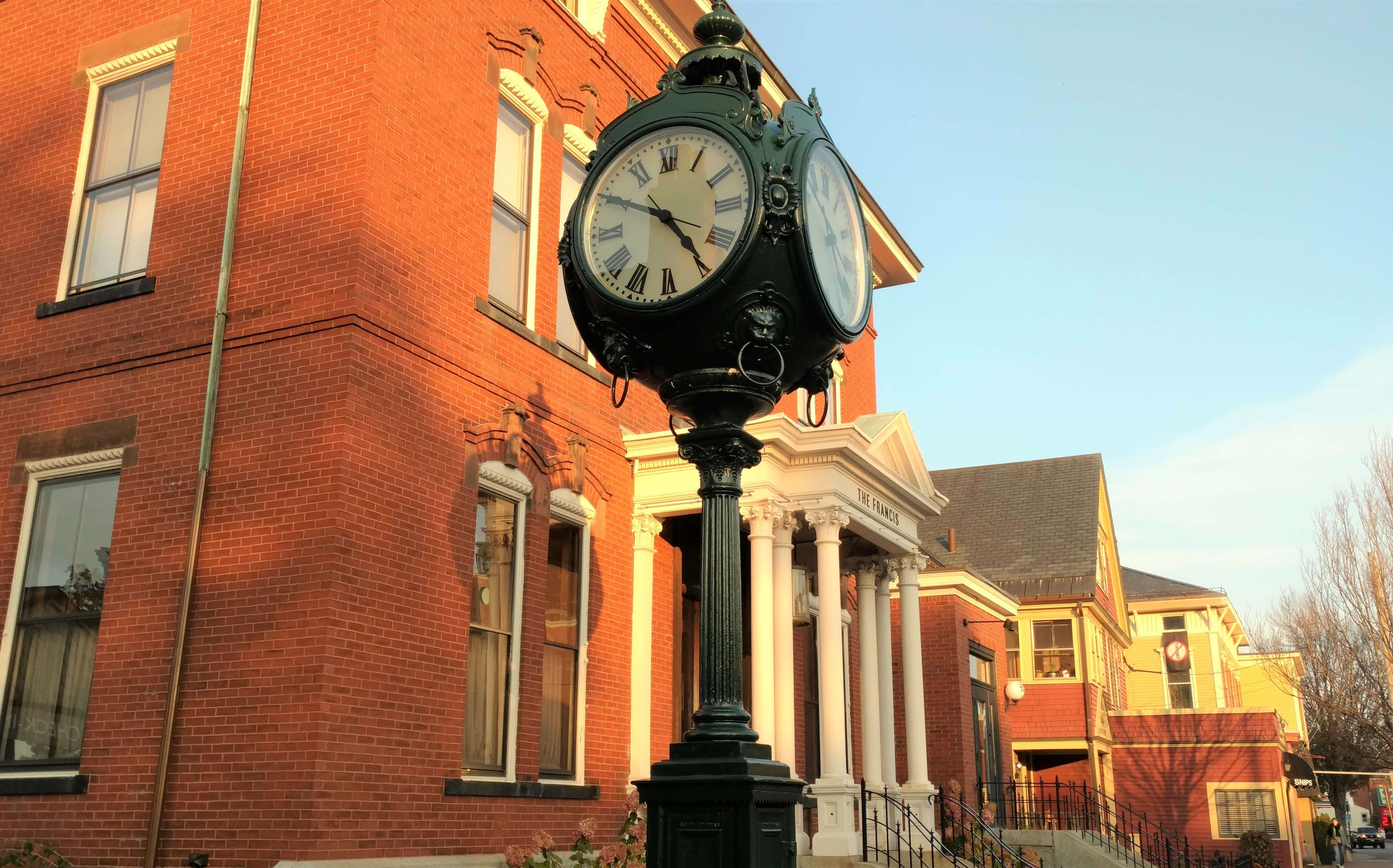 historic outdoor clock on street, in front of red brick victorian house