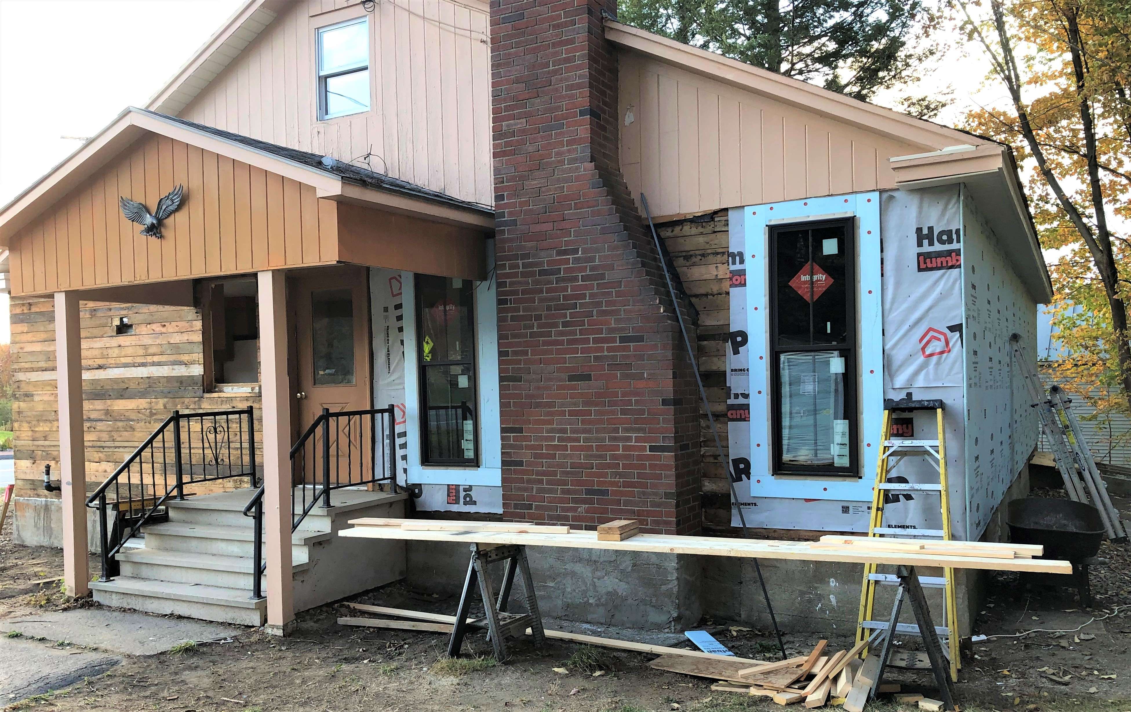 A small home with new windows constructin siding and construction equipment around it