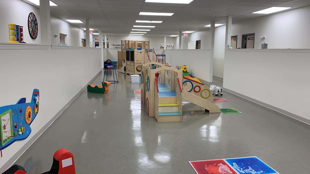 a day care space with children's wooden climbing features and colorful mats in a high-ceiling white room