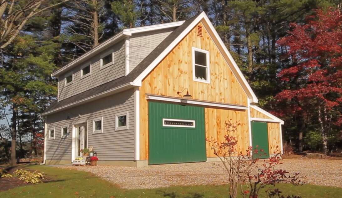 a building that looks colonial on one side, but has bare barnboard with a green door on the other side