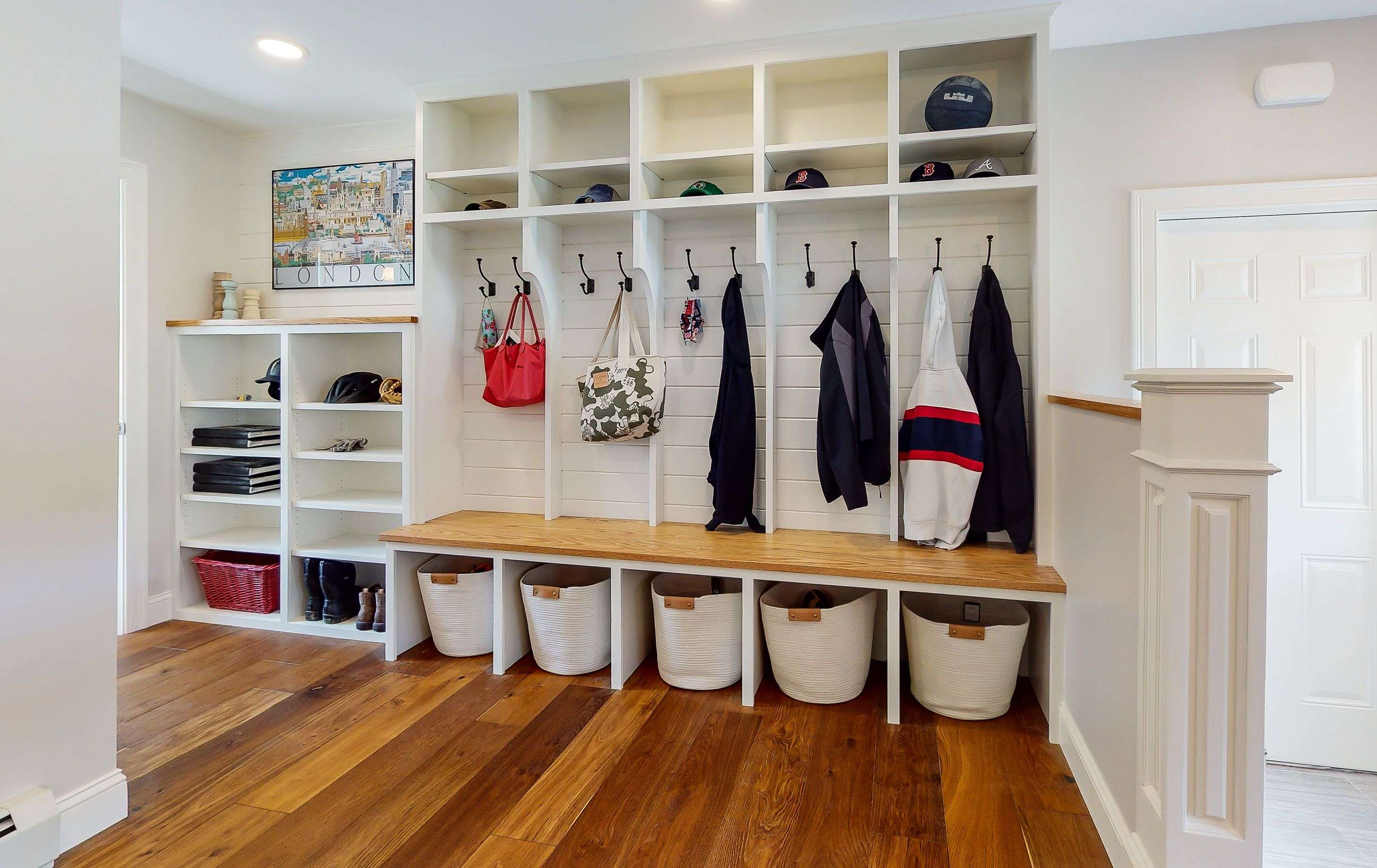 A bright mudroom with cubbies with coats hanging in them and further storage and a wood floor