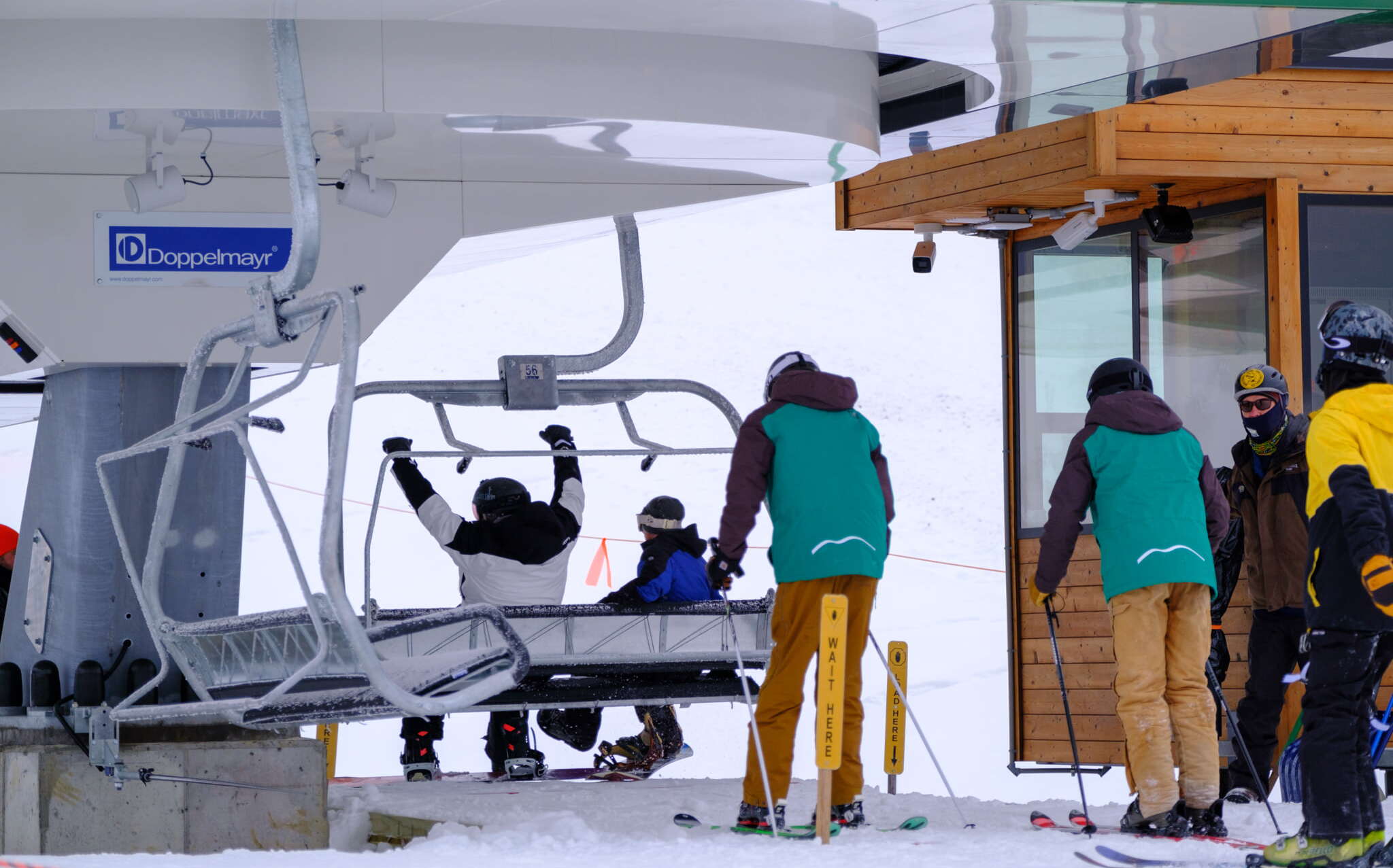 people getting on a ski lift with their arms raised in triump with a snowy mountain in the background
