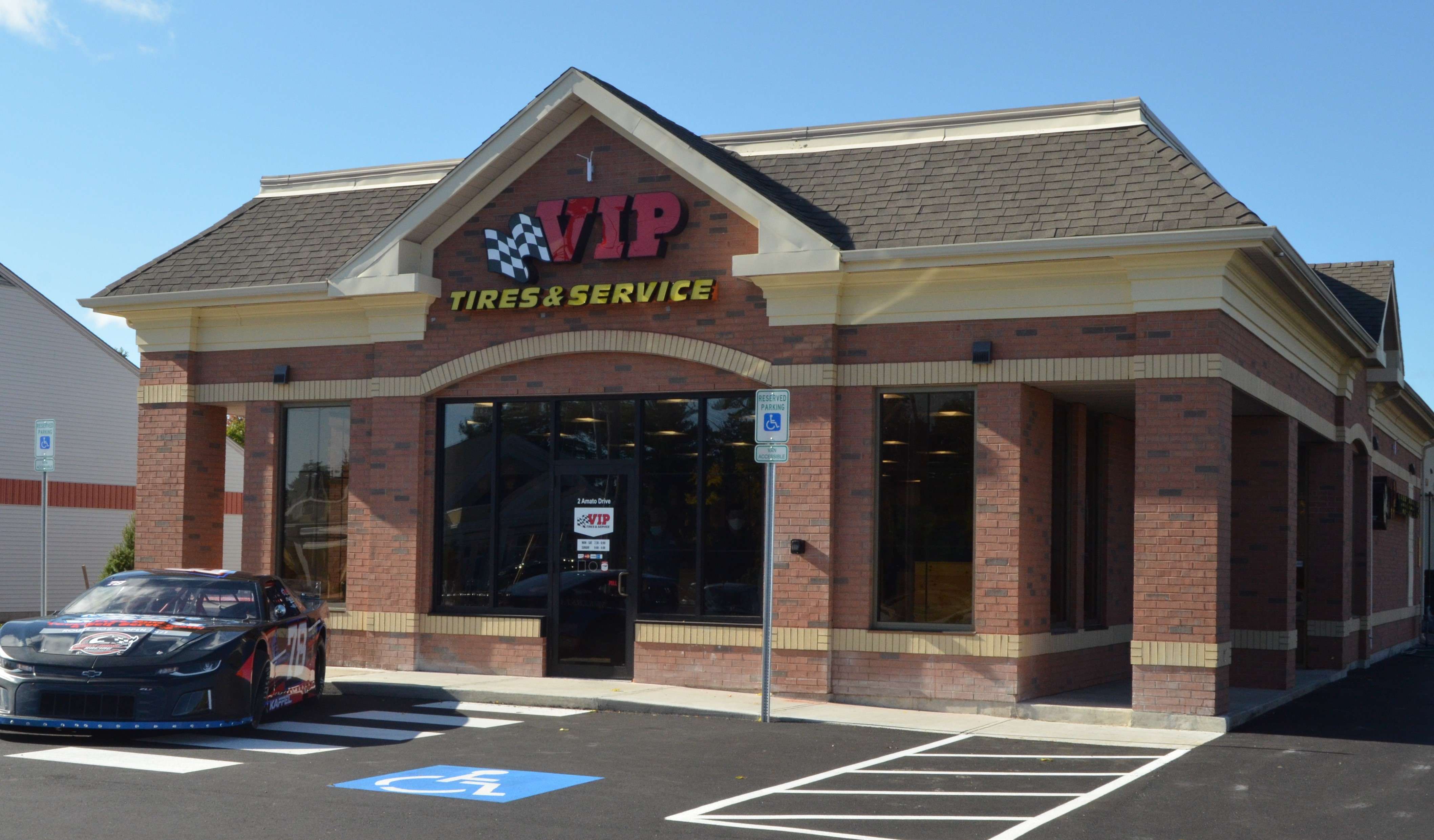 A small brick building with a sign that says VIP Tires & Service and a racing care parked out front