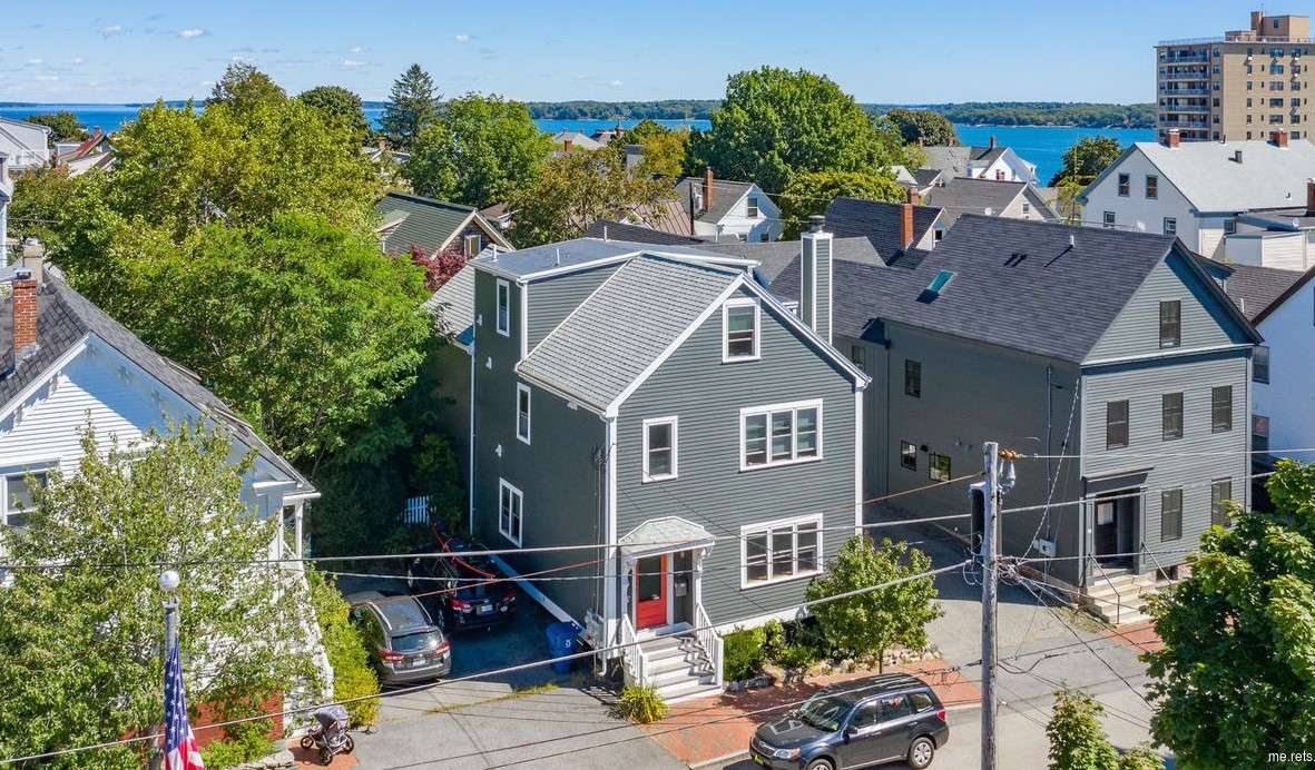 A row of clapboard three-story buildings with the one in the center a clean-looking gray with bright red door and the ocean in the background