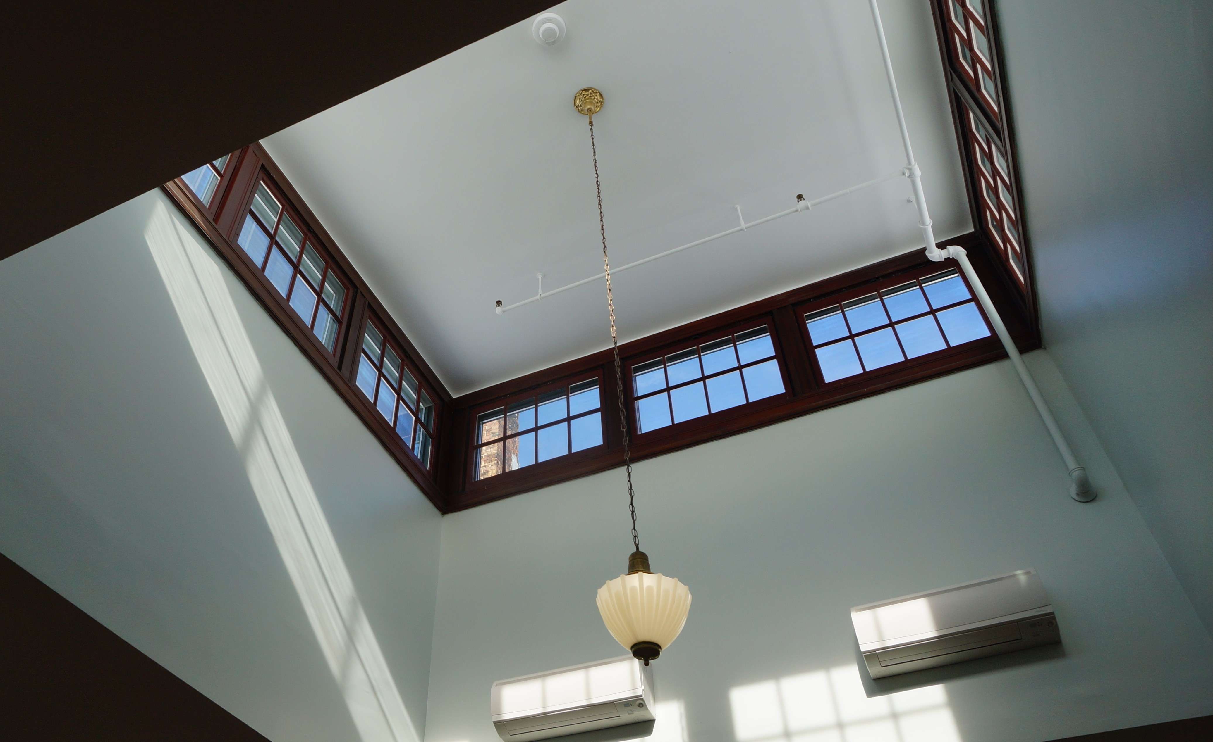 a square ceiling dome with windows around the top and a chandelier hanging from the top, two heat pumps ont he wall and sunlight from the windows