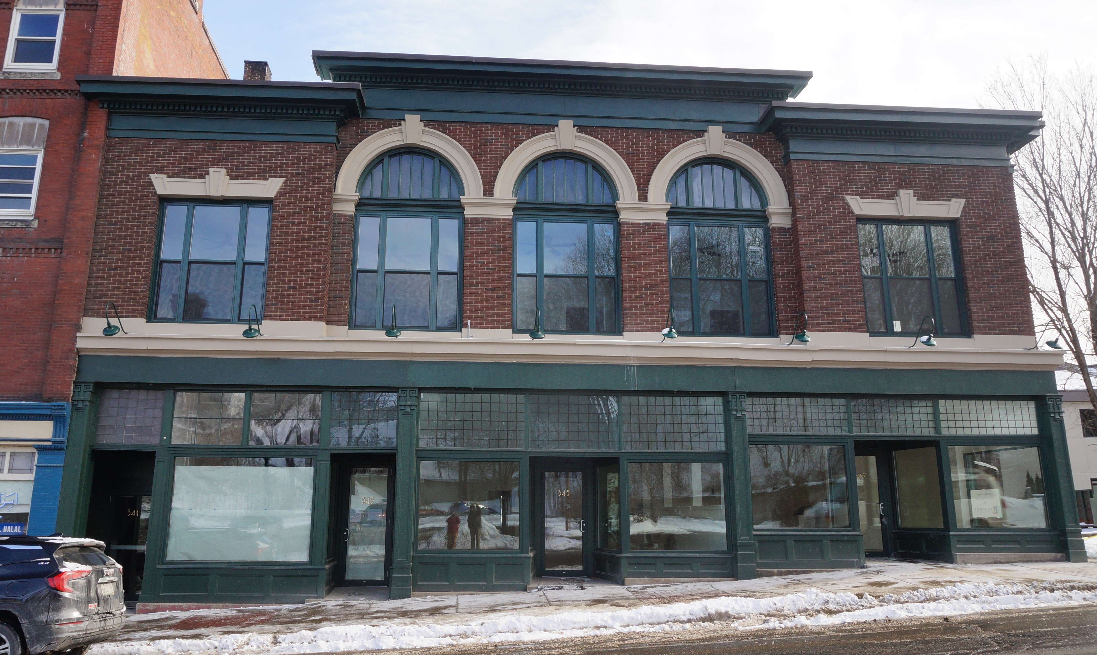 A two story building with large glass storefront windows on the first floor and big ornate arched winows on the second floor.