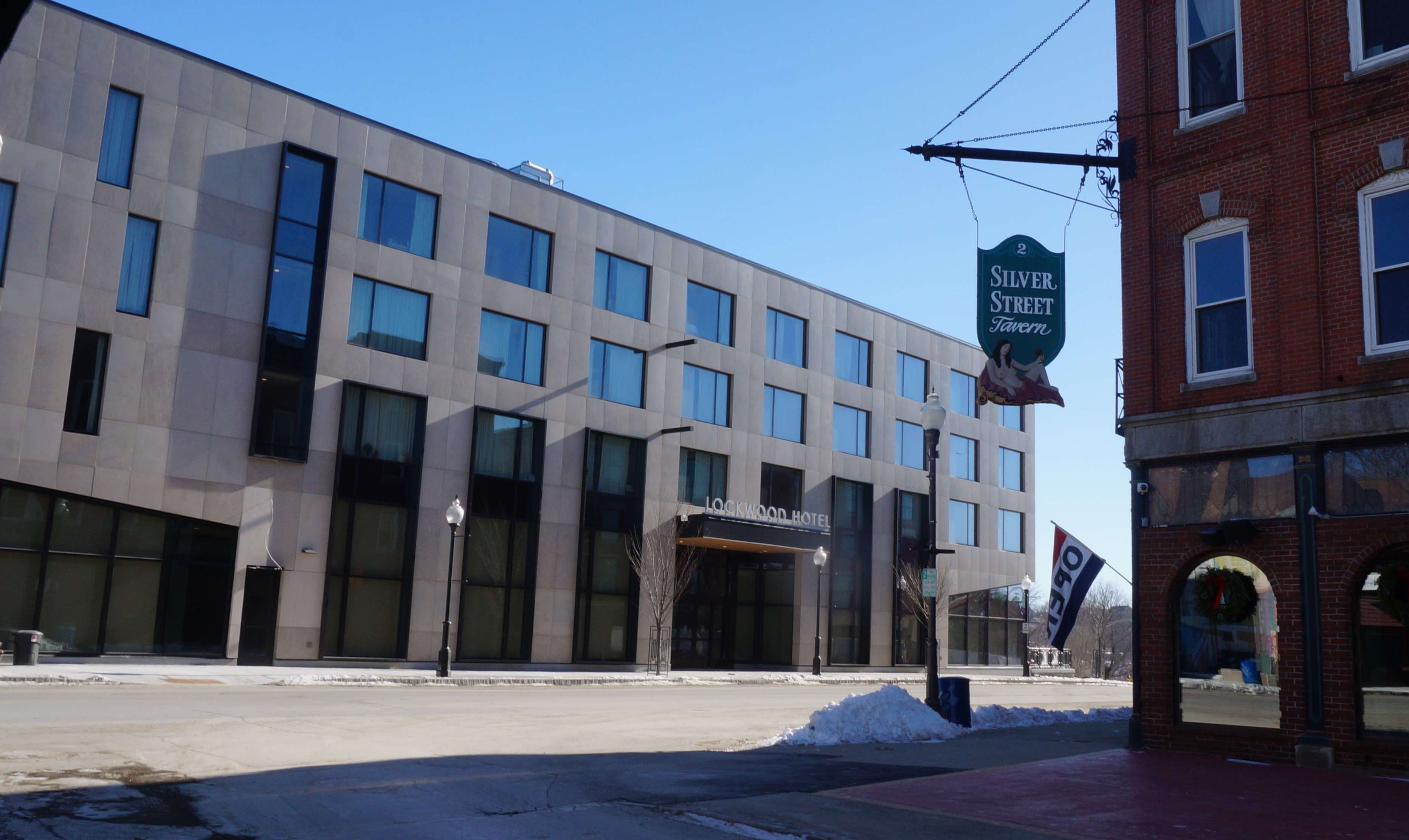 a modern four-story building on a narrow street, with an older brick building across the street the modern building has a sign the Lockwood Hotel