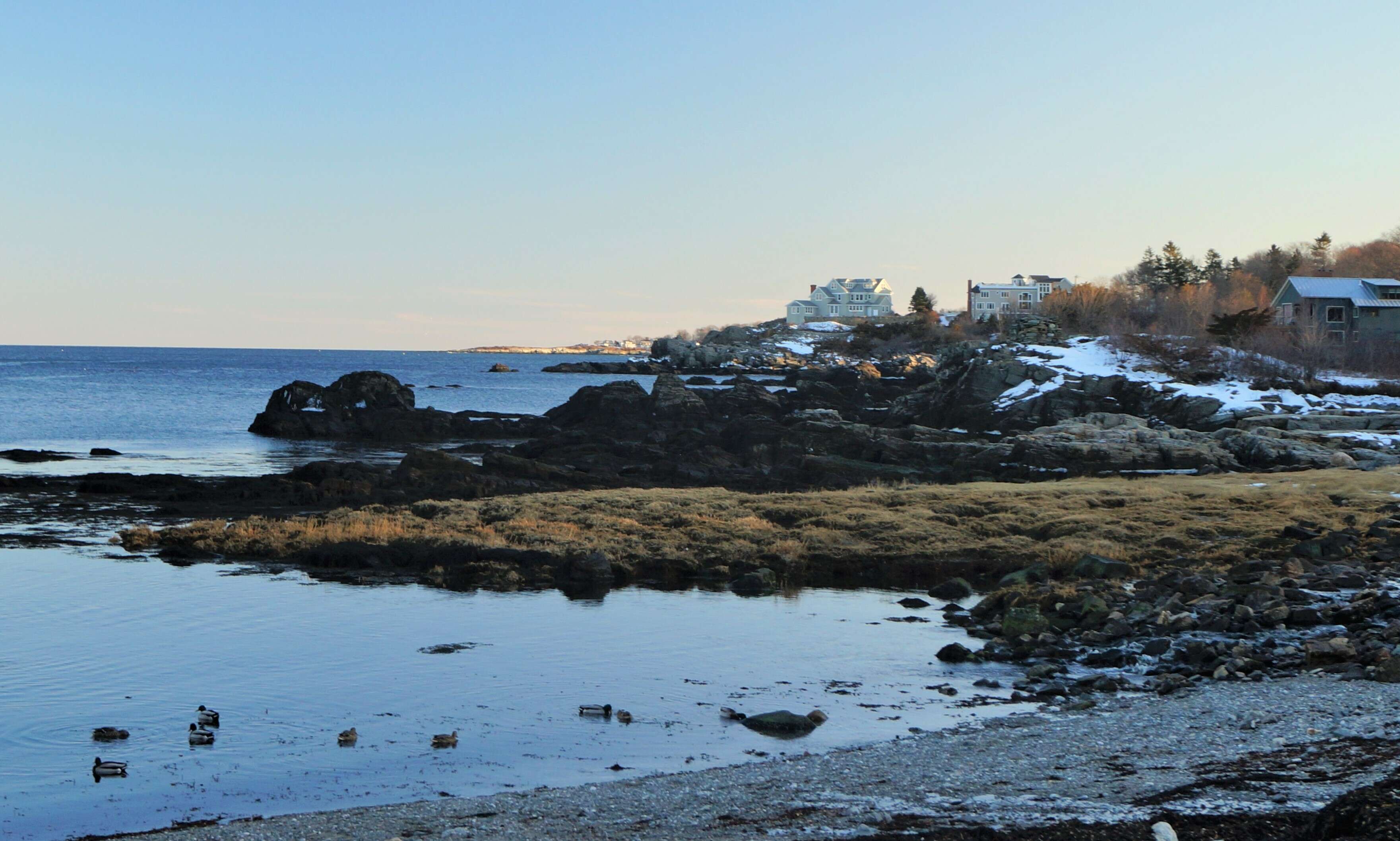 a rocky coast with a couple large expensive looking houses on a promontory in the distance