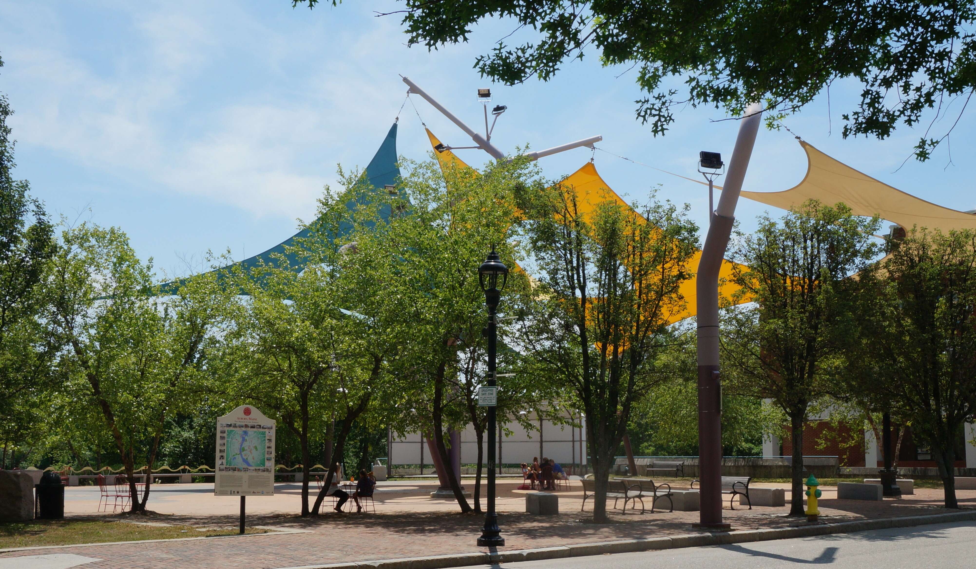 a brick plaza with bright colored canopies in the many trees and benches and picnic tables