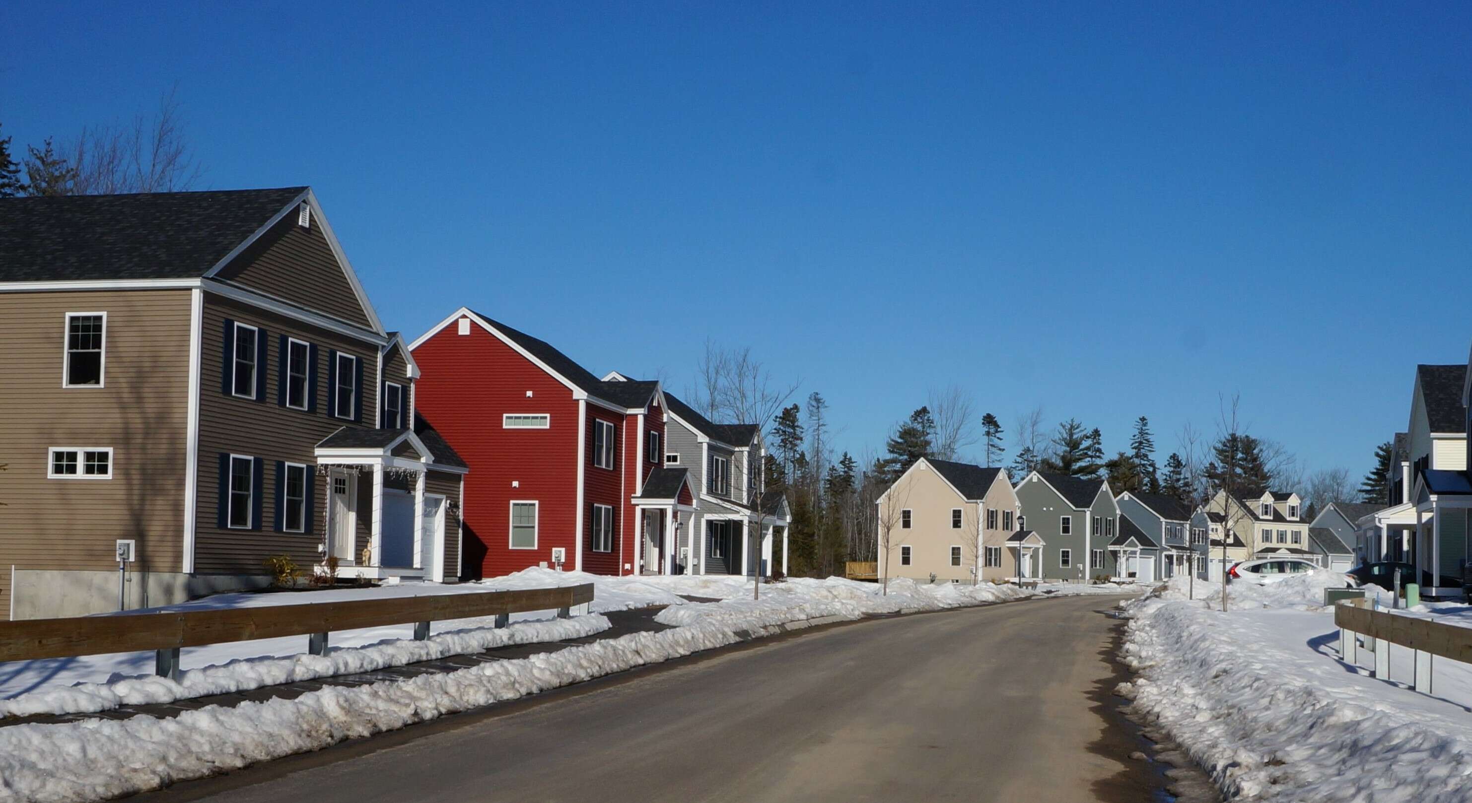 A row of brand two-story new houses in different colors with snow along the road