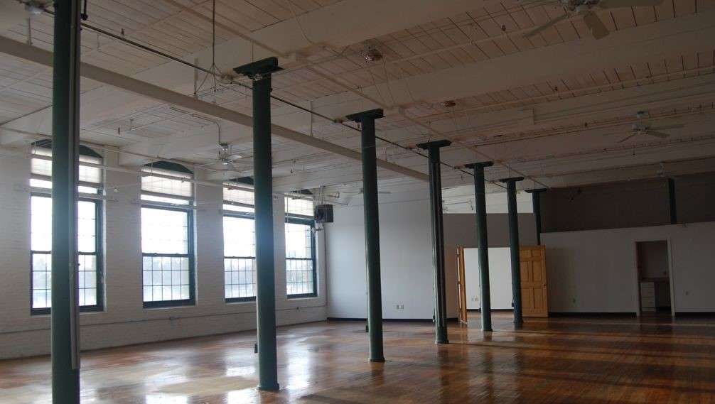 an empty industrial type room with high seilings and large windows, wooden floors and white walls