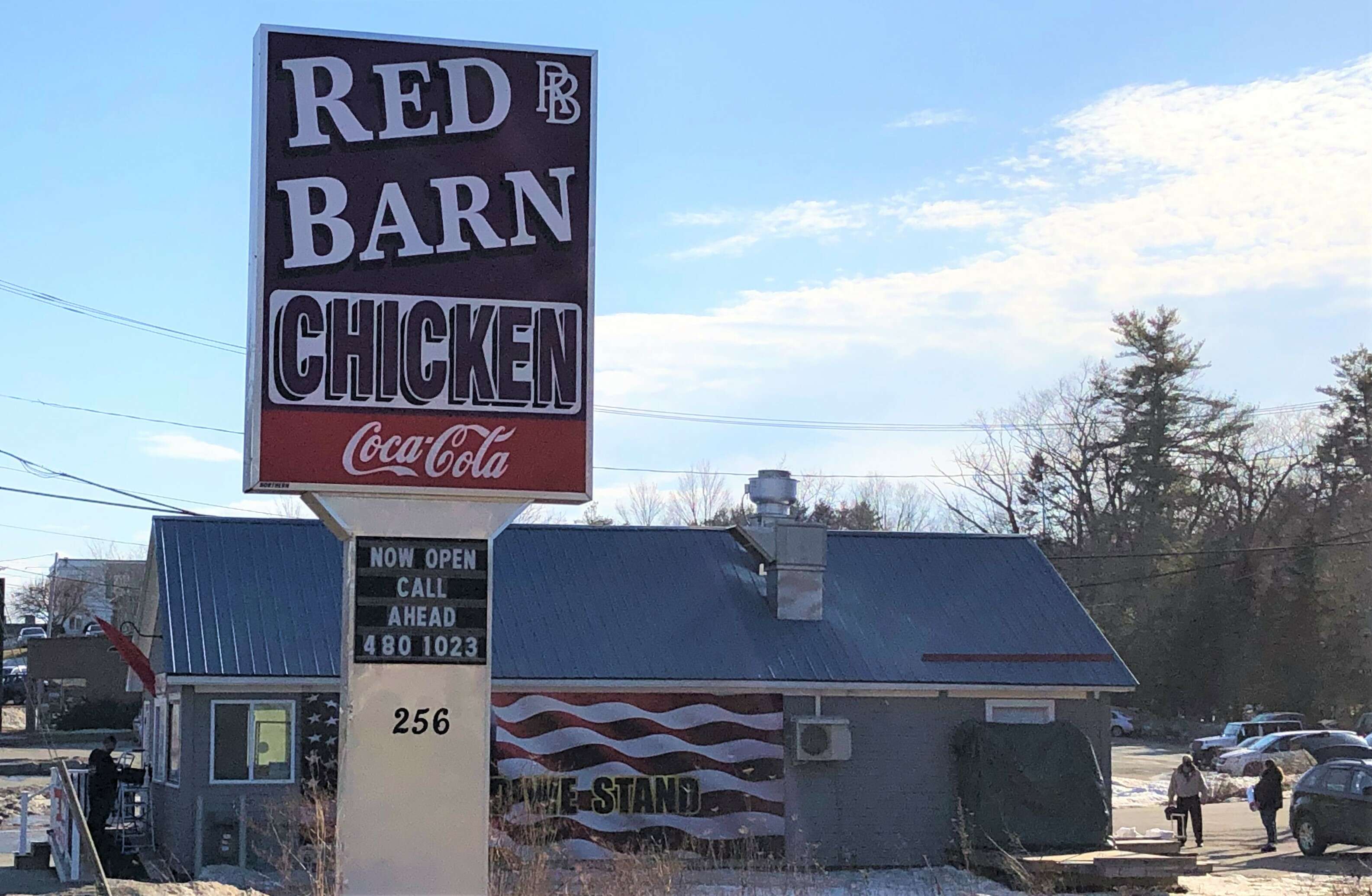 a small building with a big American flag mural on the side has a sign that says Red Barn Chicken takeout call ahead