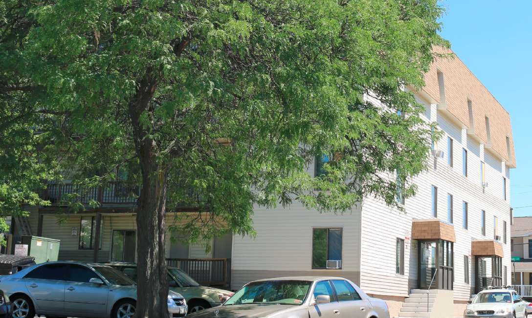 an old wooden apartment building with a big tree in front