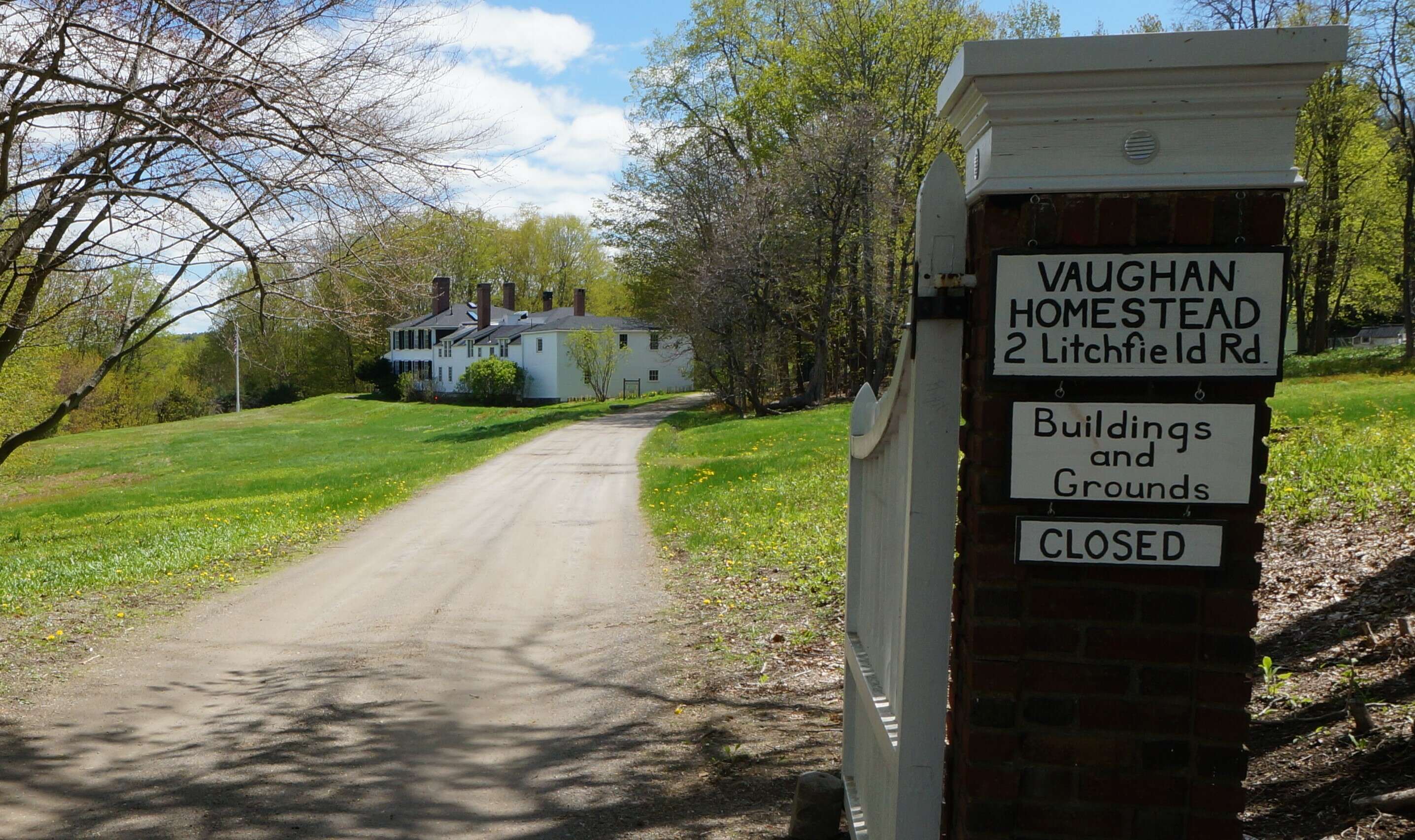 A gate with a painted sign says Vaughn Homestead and Woods 2 Litchfield road a long drive winds down to a large white colonial house on a grassy lawn