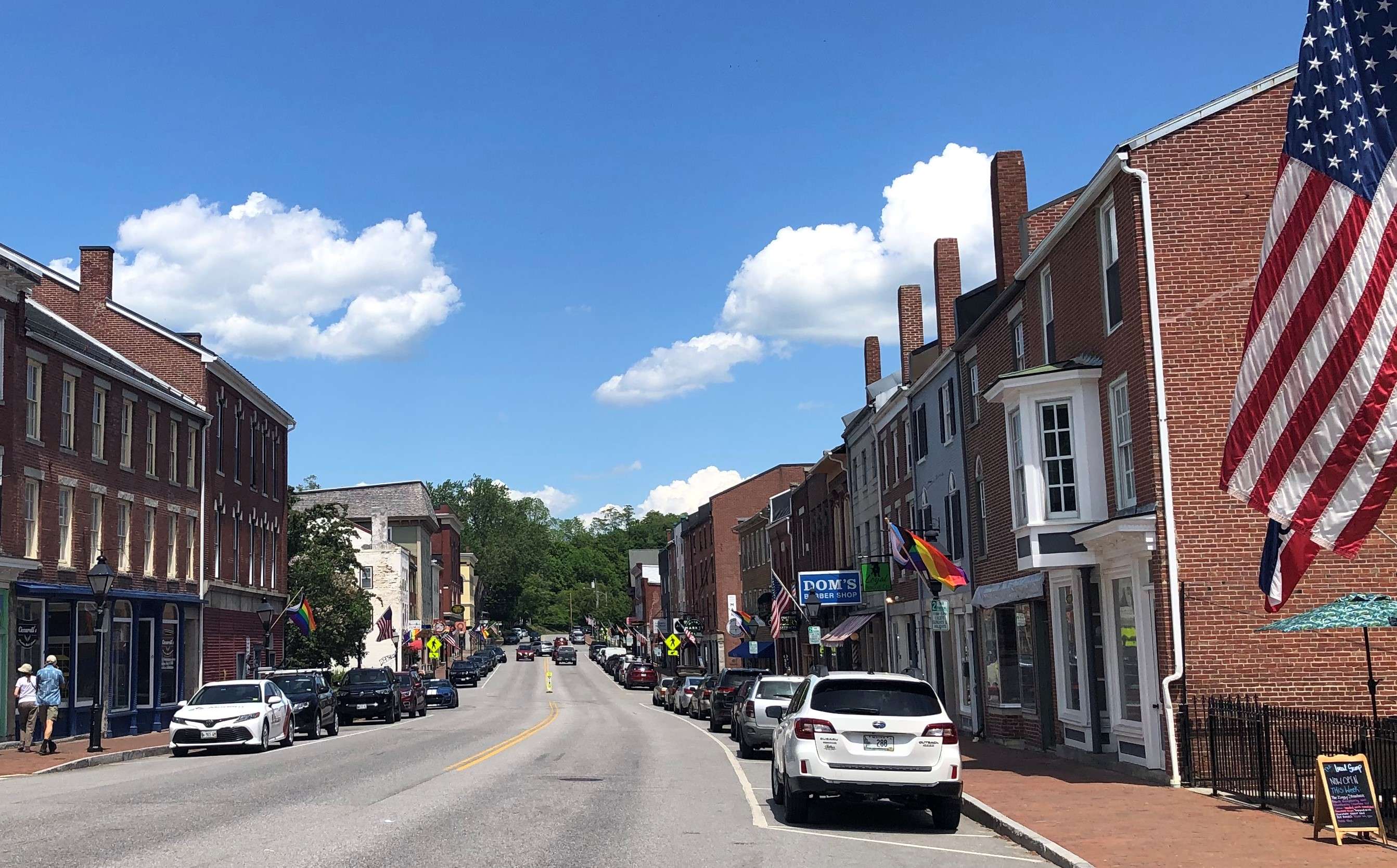 a two-lane small downtown street with brick and wooden buildings on either side and american flags on the light poles