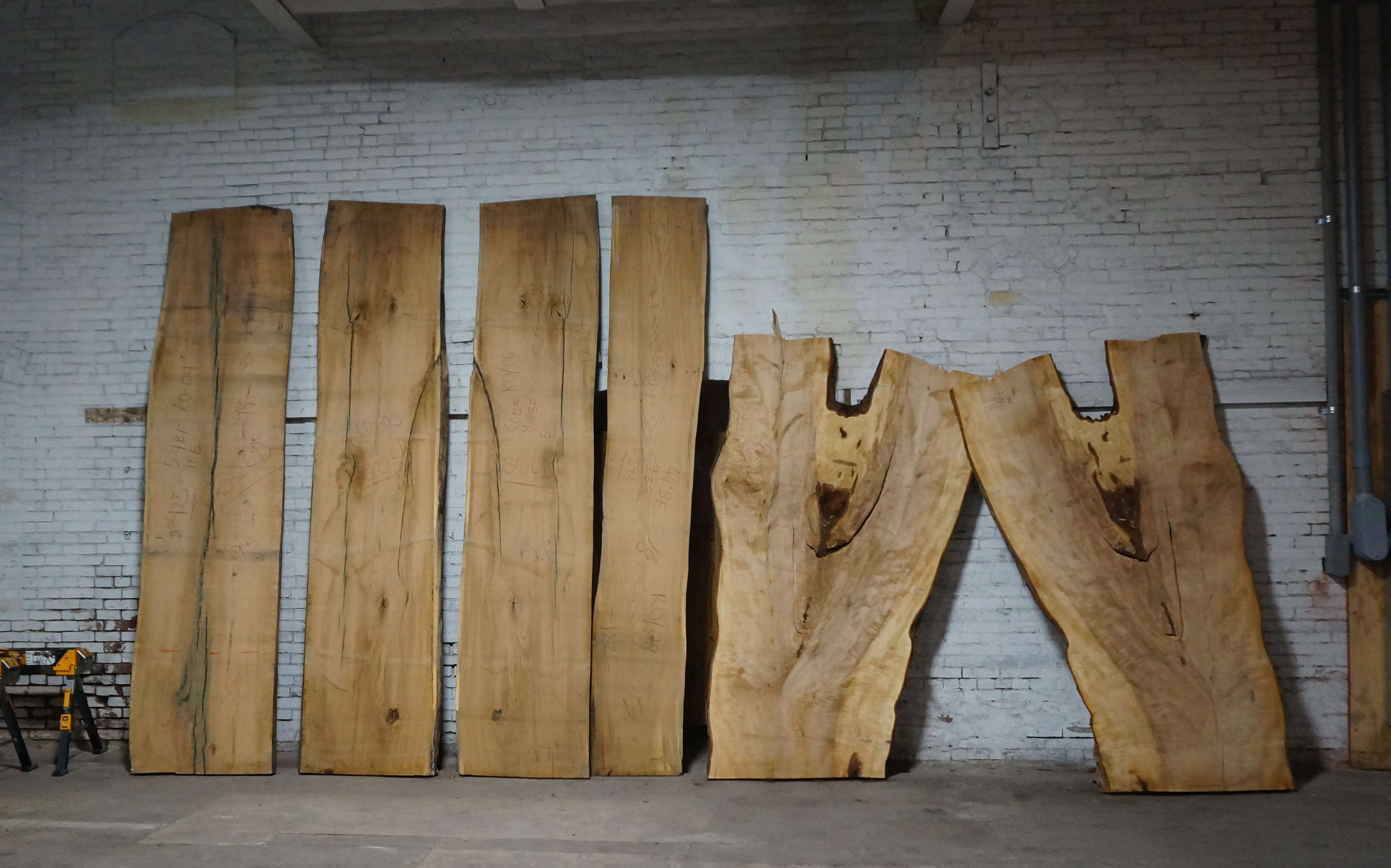 large slabs of wood, four straight and two curved with forks where branches once were, lean against a whitewashed brick wall