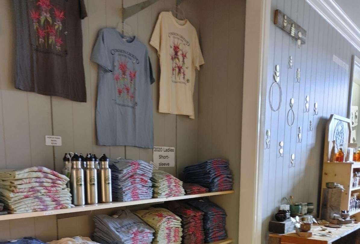 A store interior shows a wall with T-shirts that say Common Ground Country Fair with more folded on shevels below and another items in the background