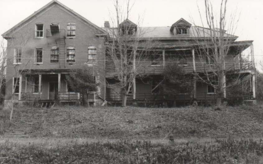 B/W view of crumbling brick building, overgrown with trees and shrubs