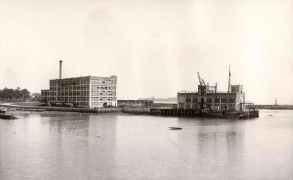 black and white photo of factory and adjacent building on wharf