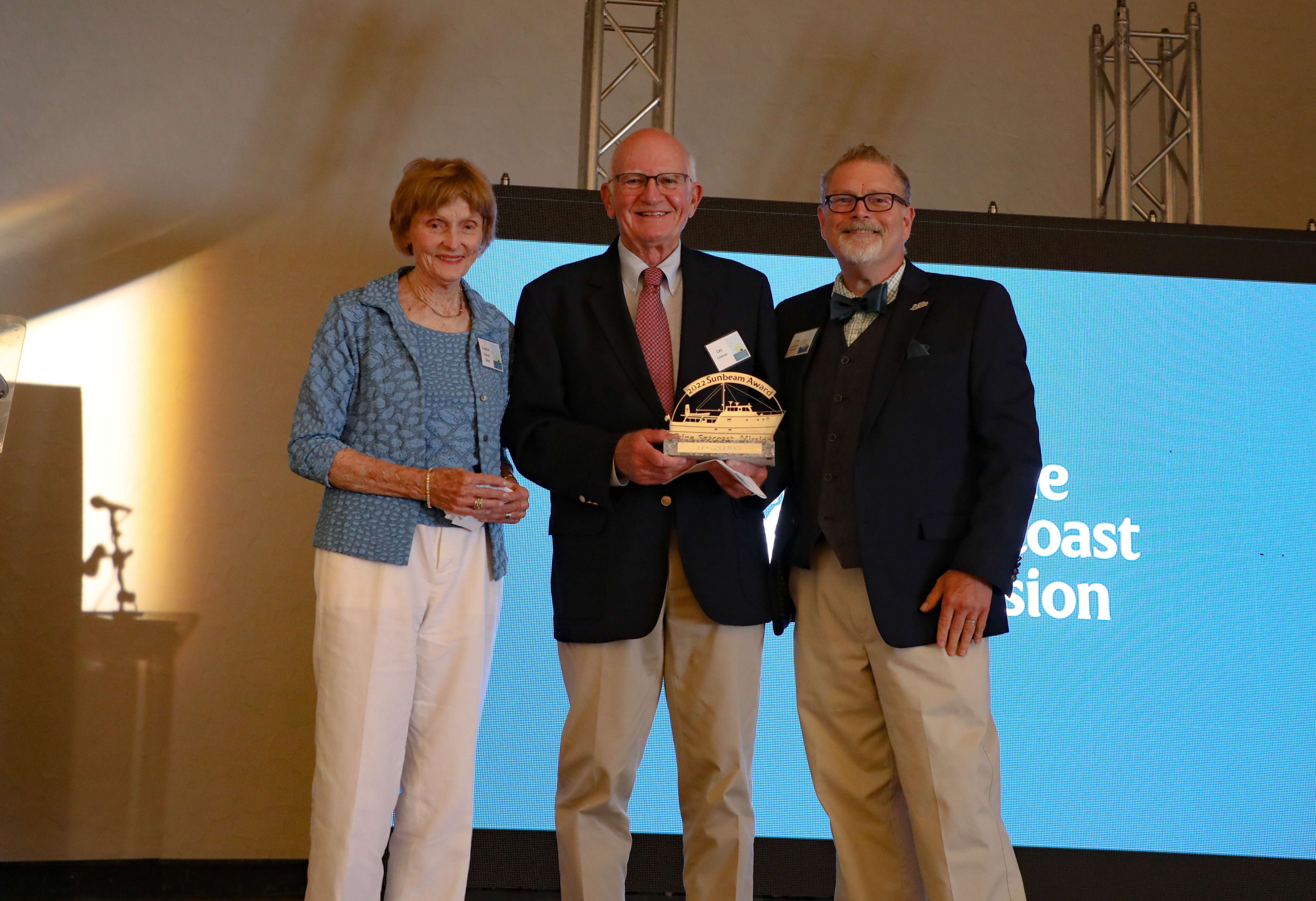 3 people with screen and award smiling