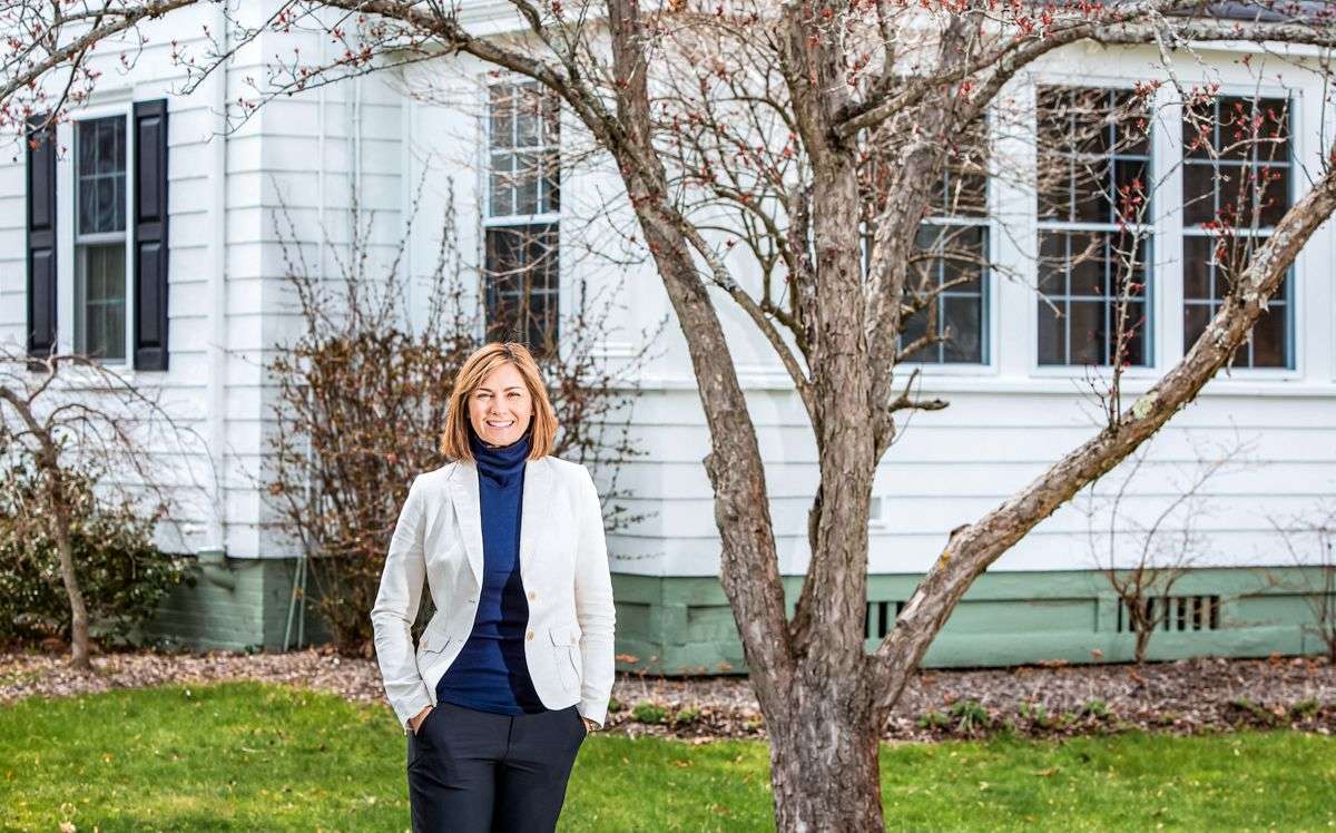 person smiling in white jacket in front of house and tree