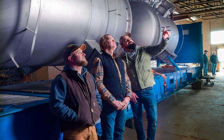 3 people looking up next to big piece of equipment