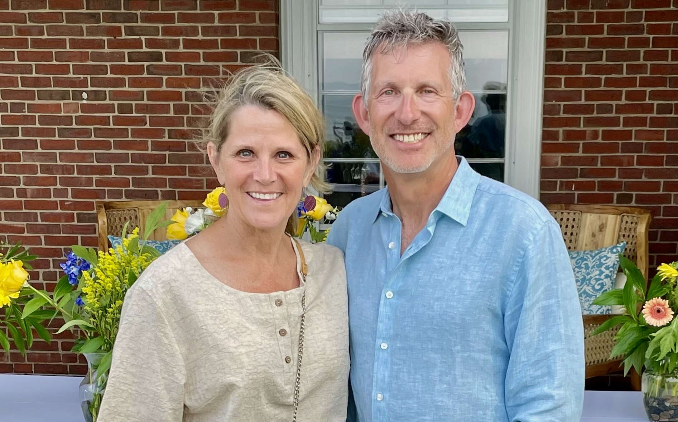 2 people standing in front of brick wall and flowers