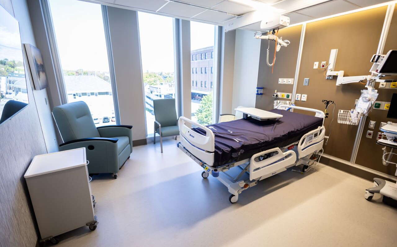 A room has a hospital bed and chars and medical equipment plus windows.