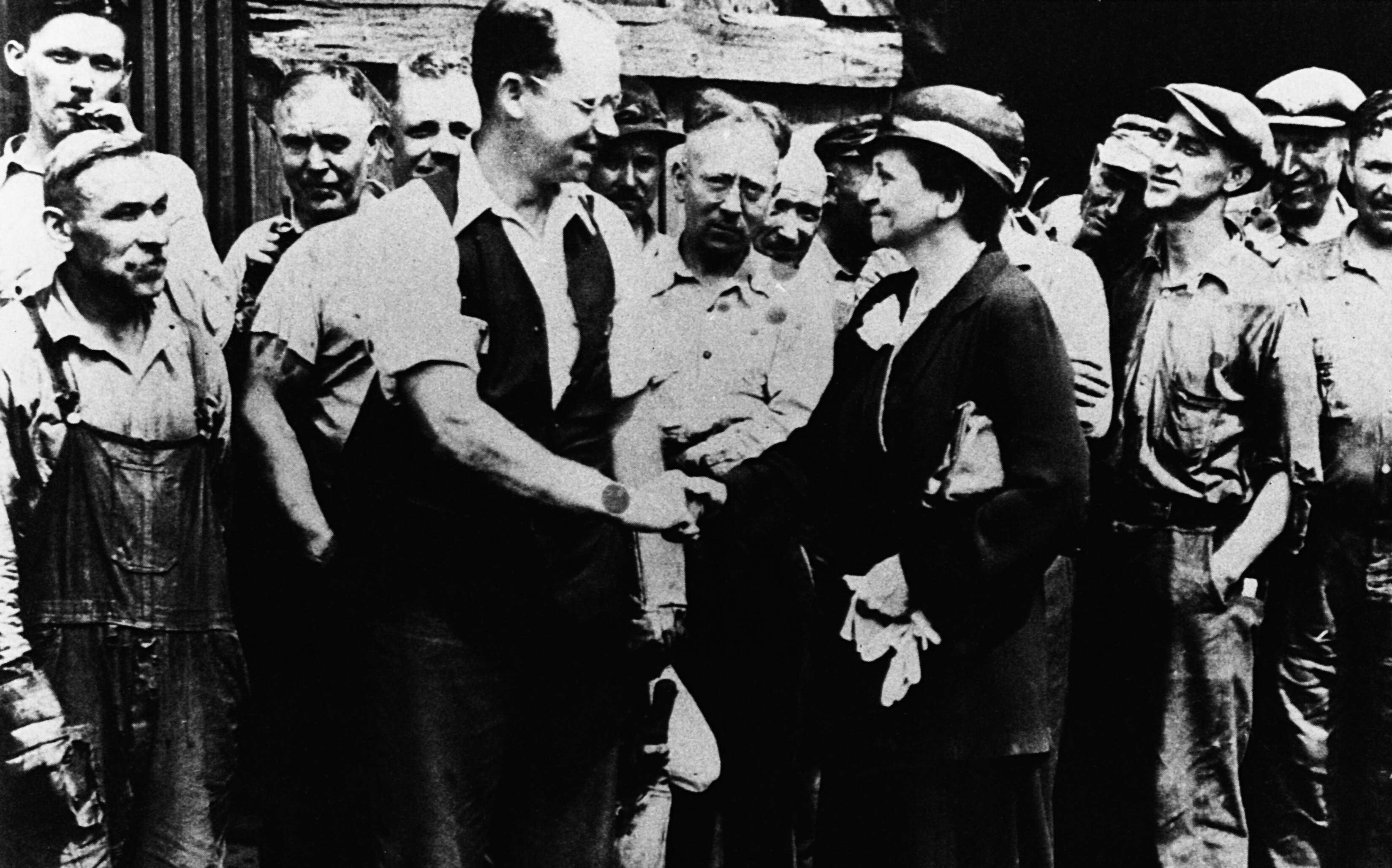 An old blakc-and-white photo shows people smiling and shaking hands.