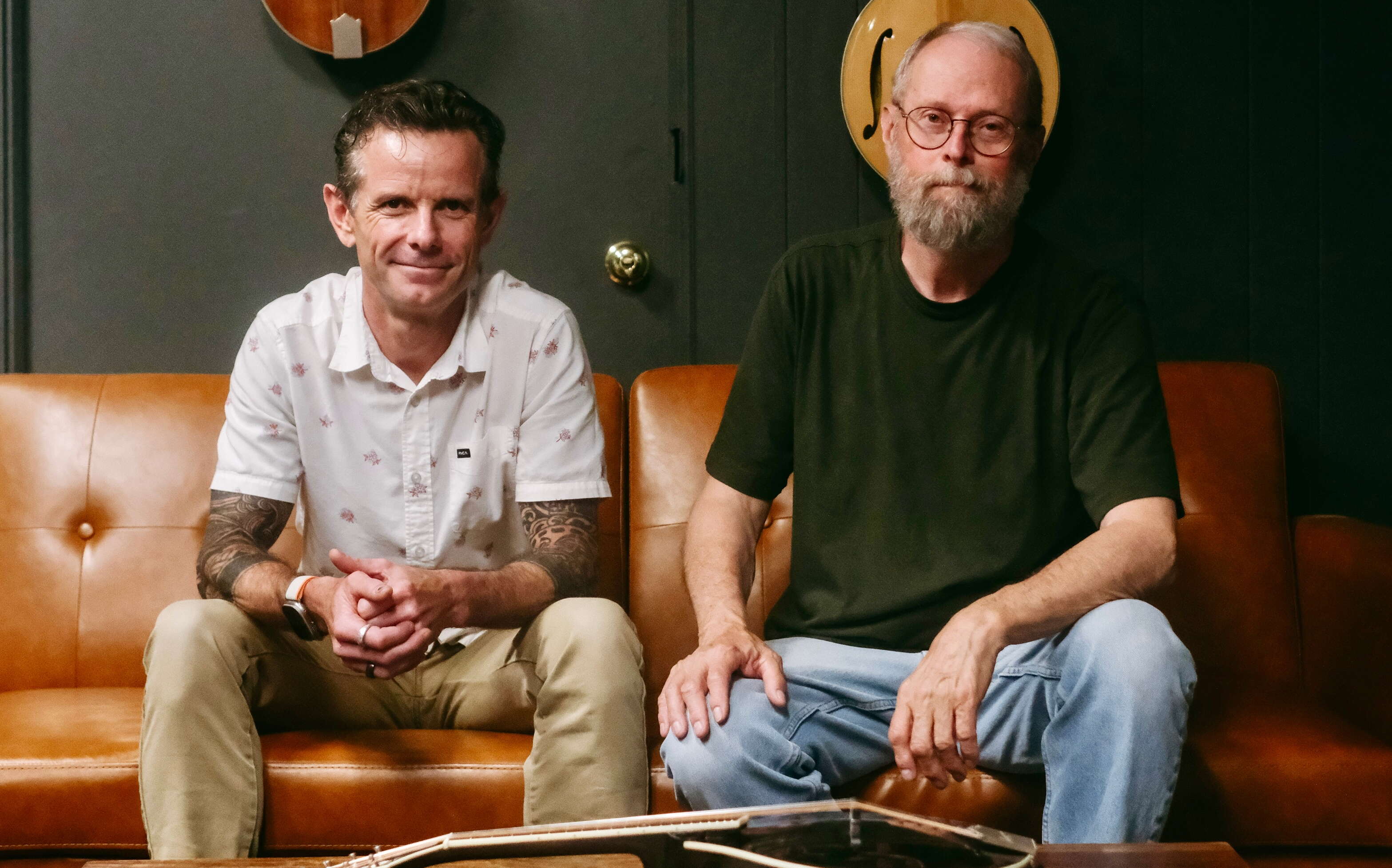 Two people with Bourgeois Guitars sit on a couch with a mandolin in front of them.