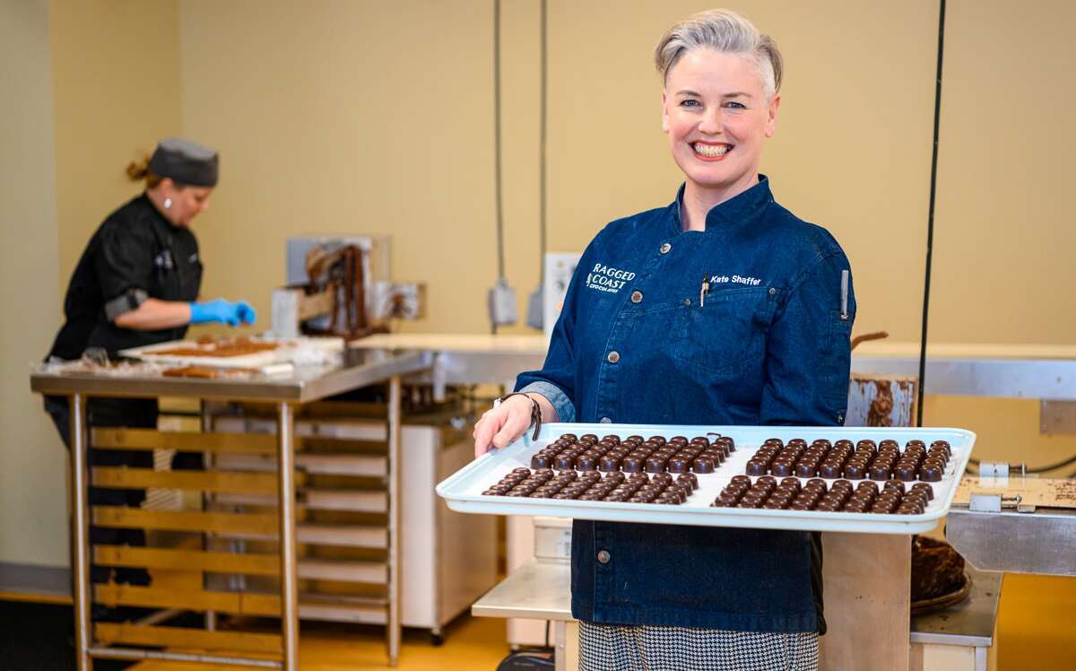 Kate Shaffer poses with a tray of chocolates while a worker works in the background.