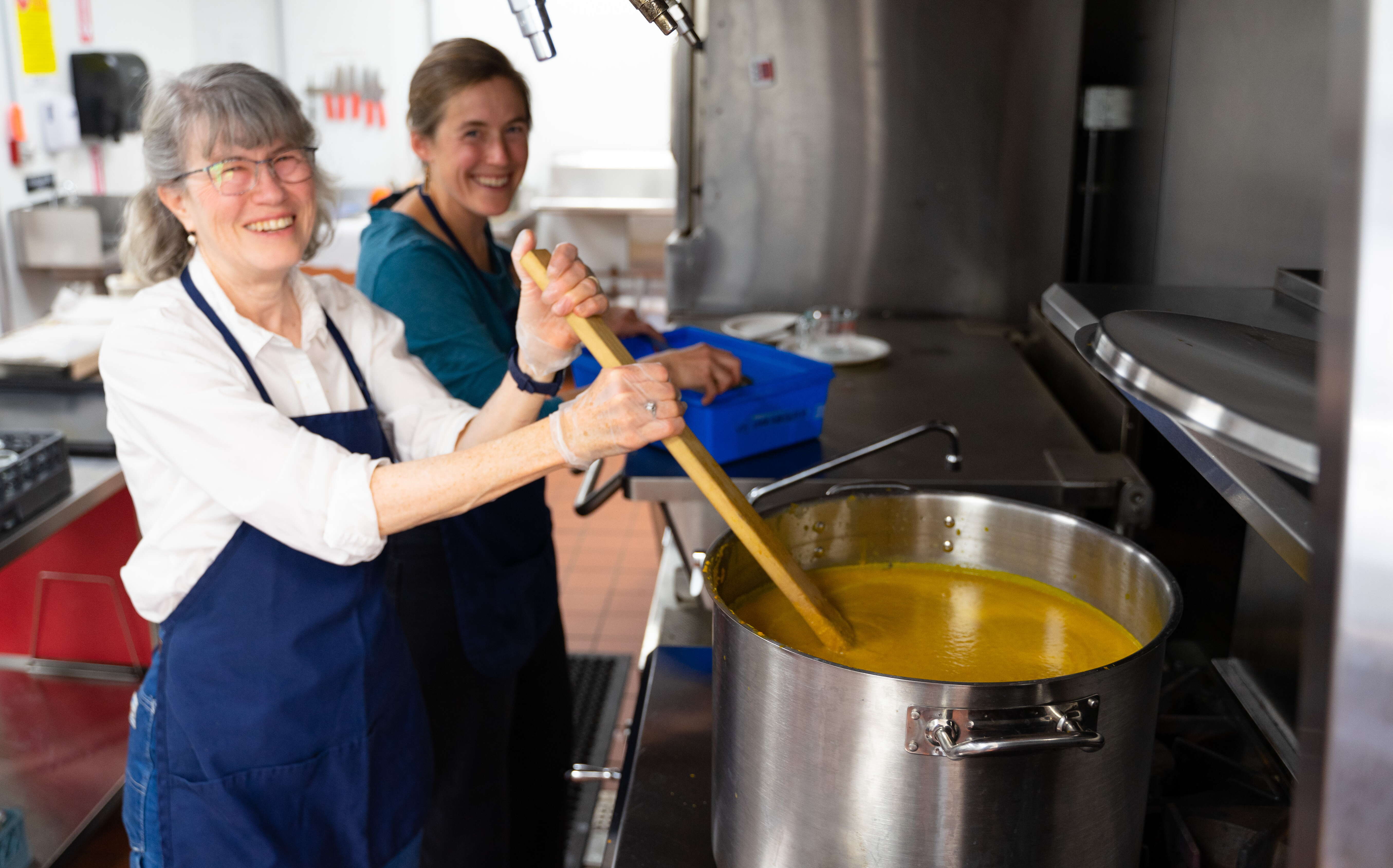 Two people stand at a stove making soup.