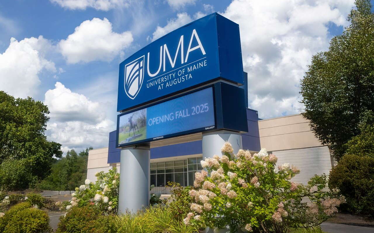 A building with a sign and flowering bushes.