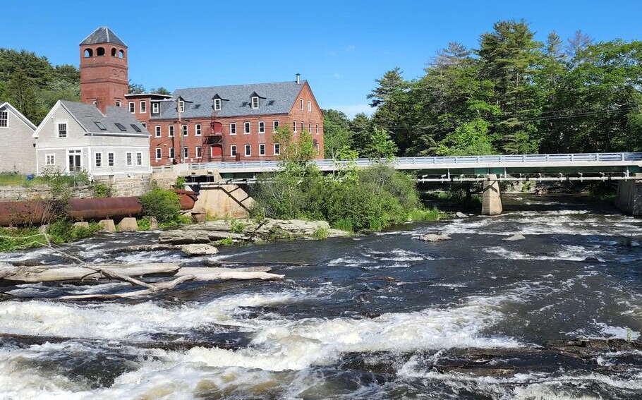 An old brick mill sits next to a river.