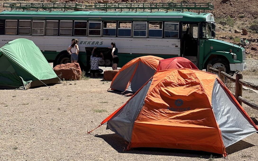 Several tents and a bus are in a desert.