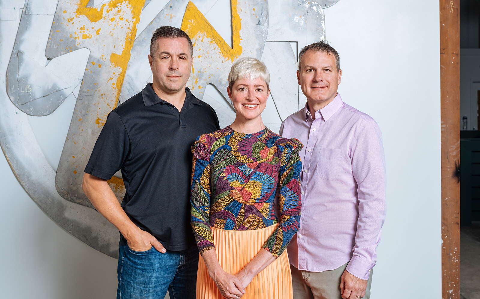 Three people pose in front of a wall.
